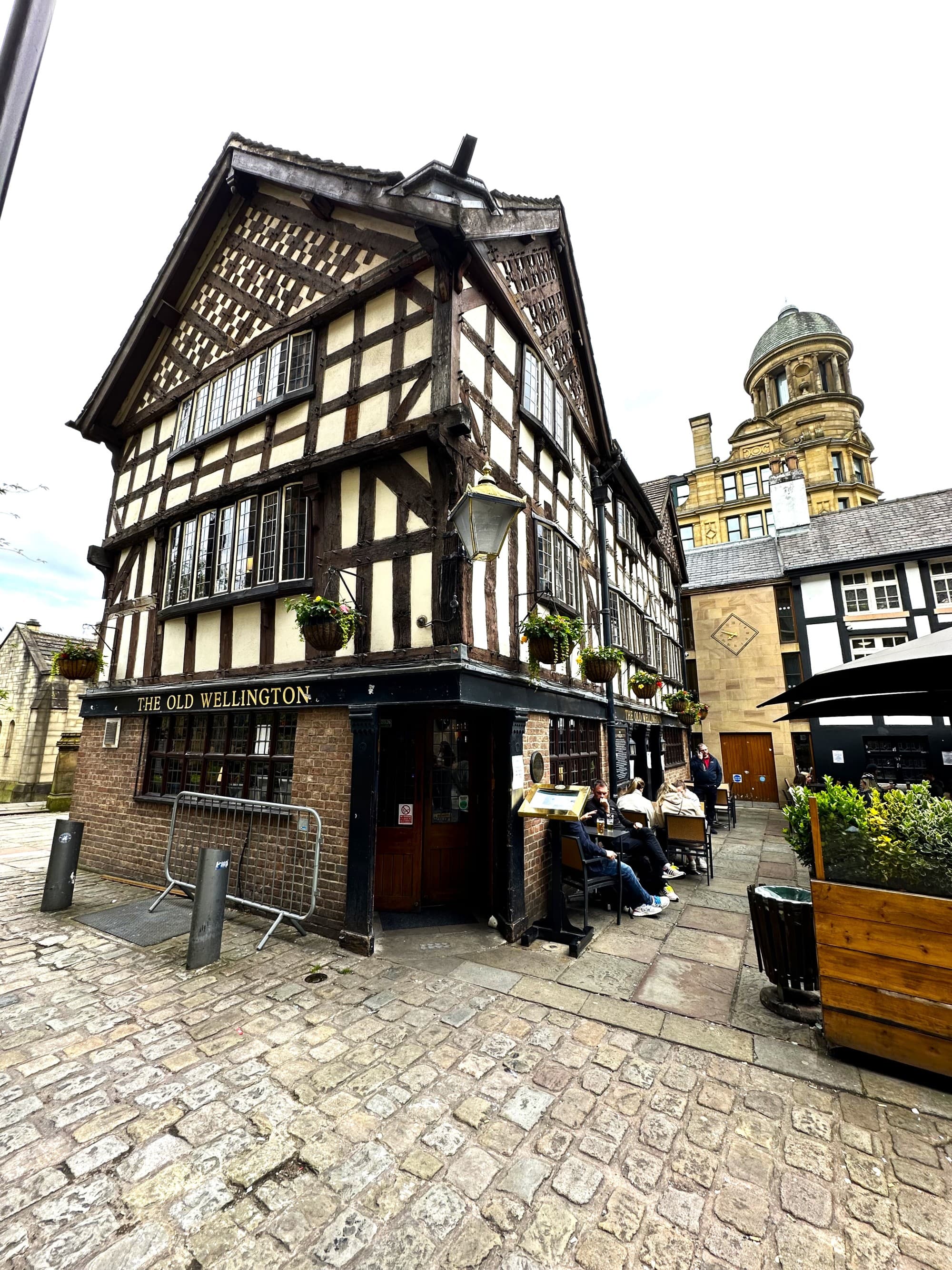 A half-timbered building with the sign “The Old Wellington” juxtaposed against modern architecture, highlighting a blend of old and new.