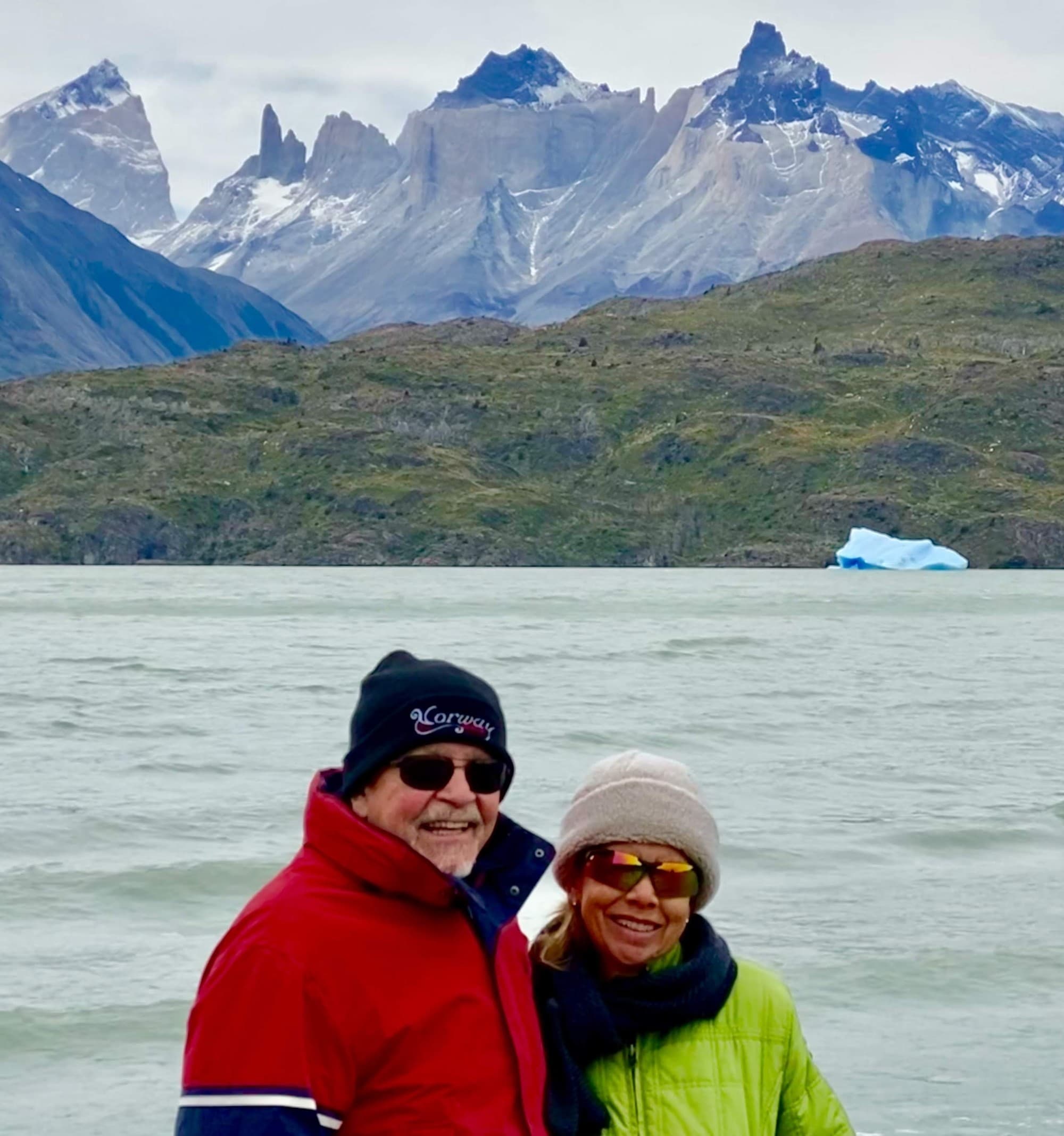 A couple posing in Patagonia in front of a body of water and snow-capped mountains on a cold day.