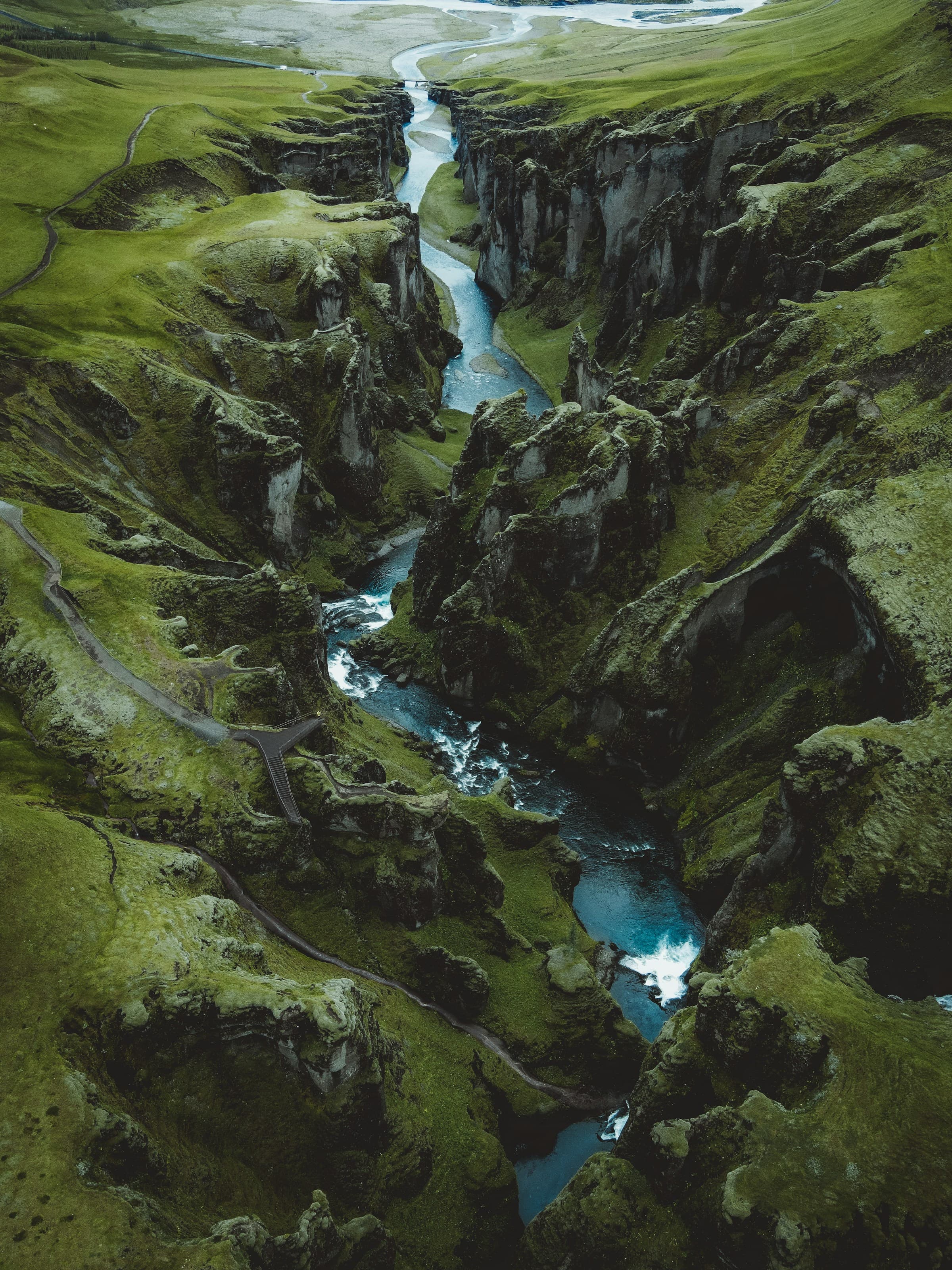 Aerial view of Fjaðrárgljúfur Canyon, with a river flowing through the center of green land.