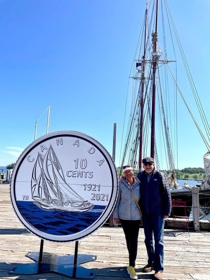 Diana and a man standing next to a giant Canadian dime in front of boats in the harbor