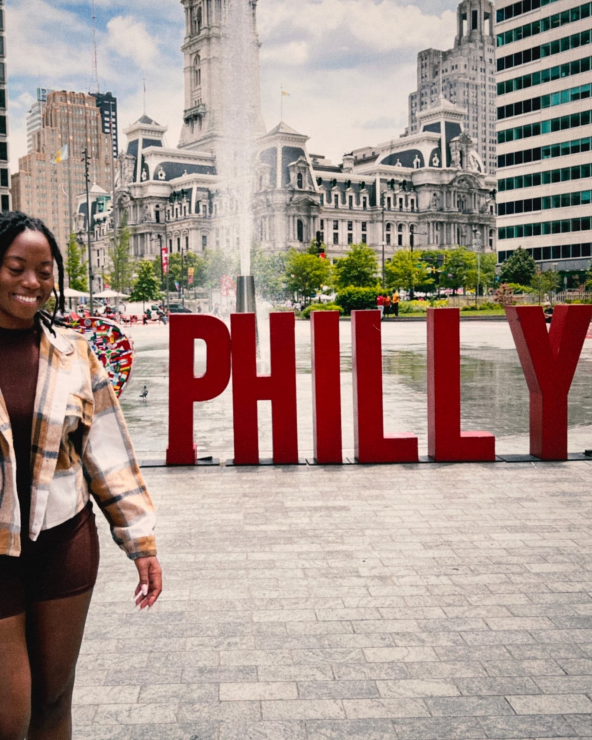 Travel advisor Ashlyn standing in front of the red PHILLY sign in the middle of the city with a fountain behind