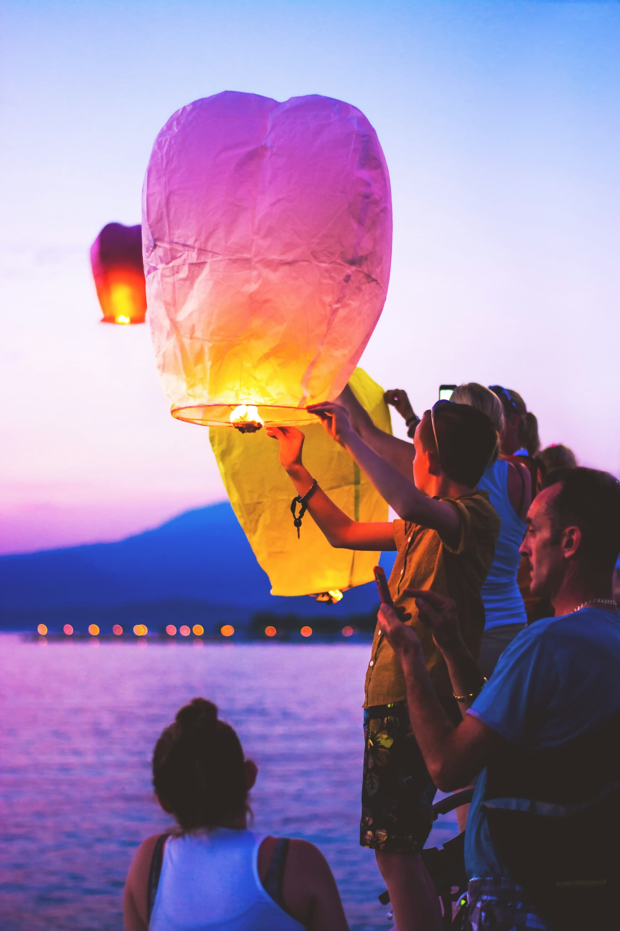 A group of people lighting a lantern next to a lake during the sunset