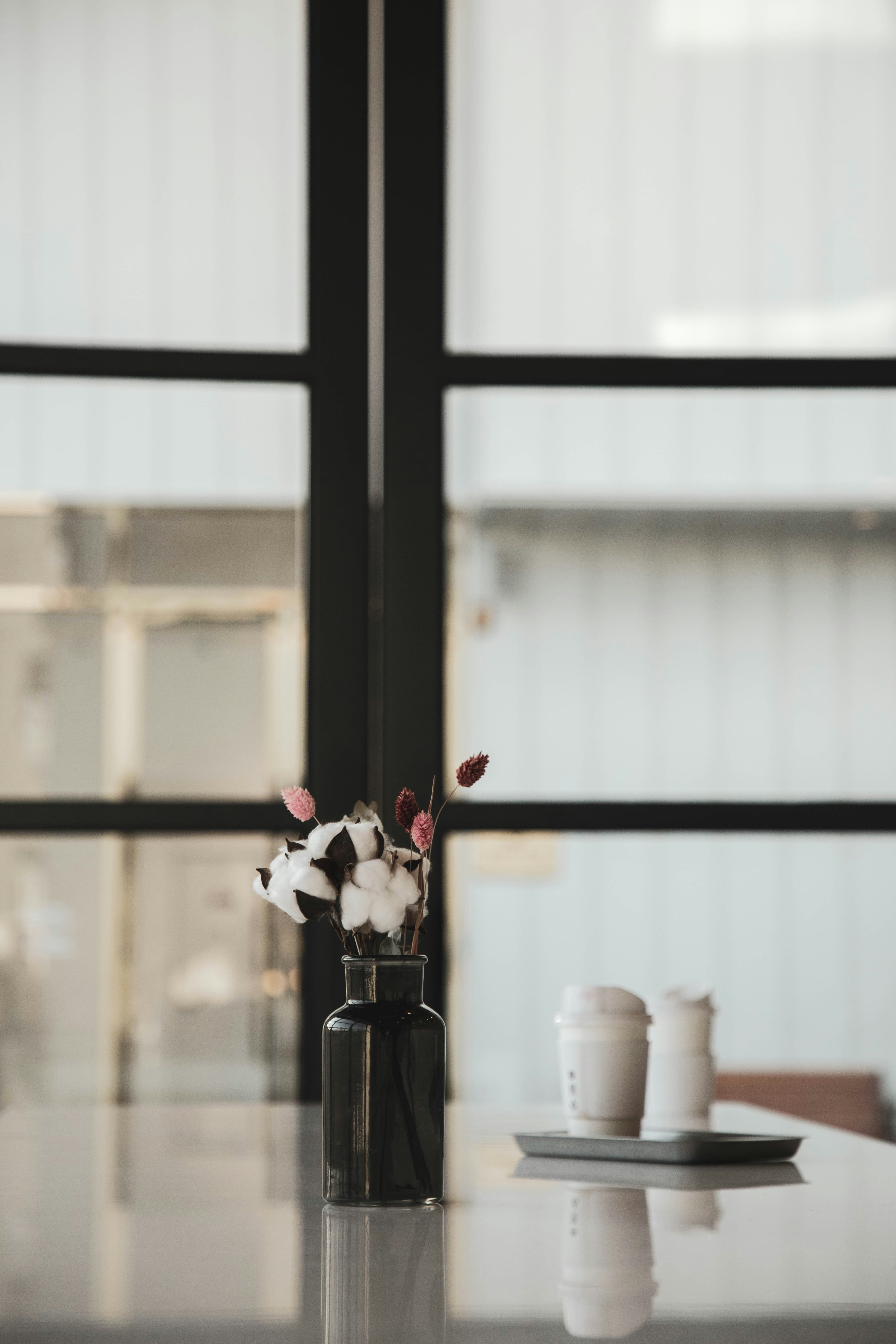 A table with coffees and flowers with a window in the background.