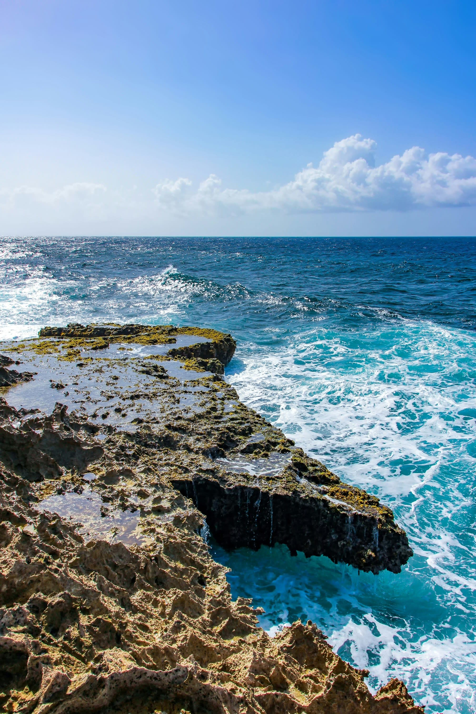 The image reveals a rugged coastline with cliffs against a vibrant blue ocean and a partly cloudy sky.