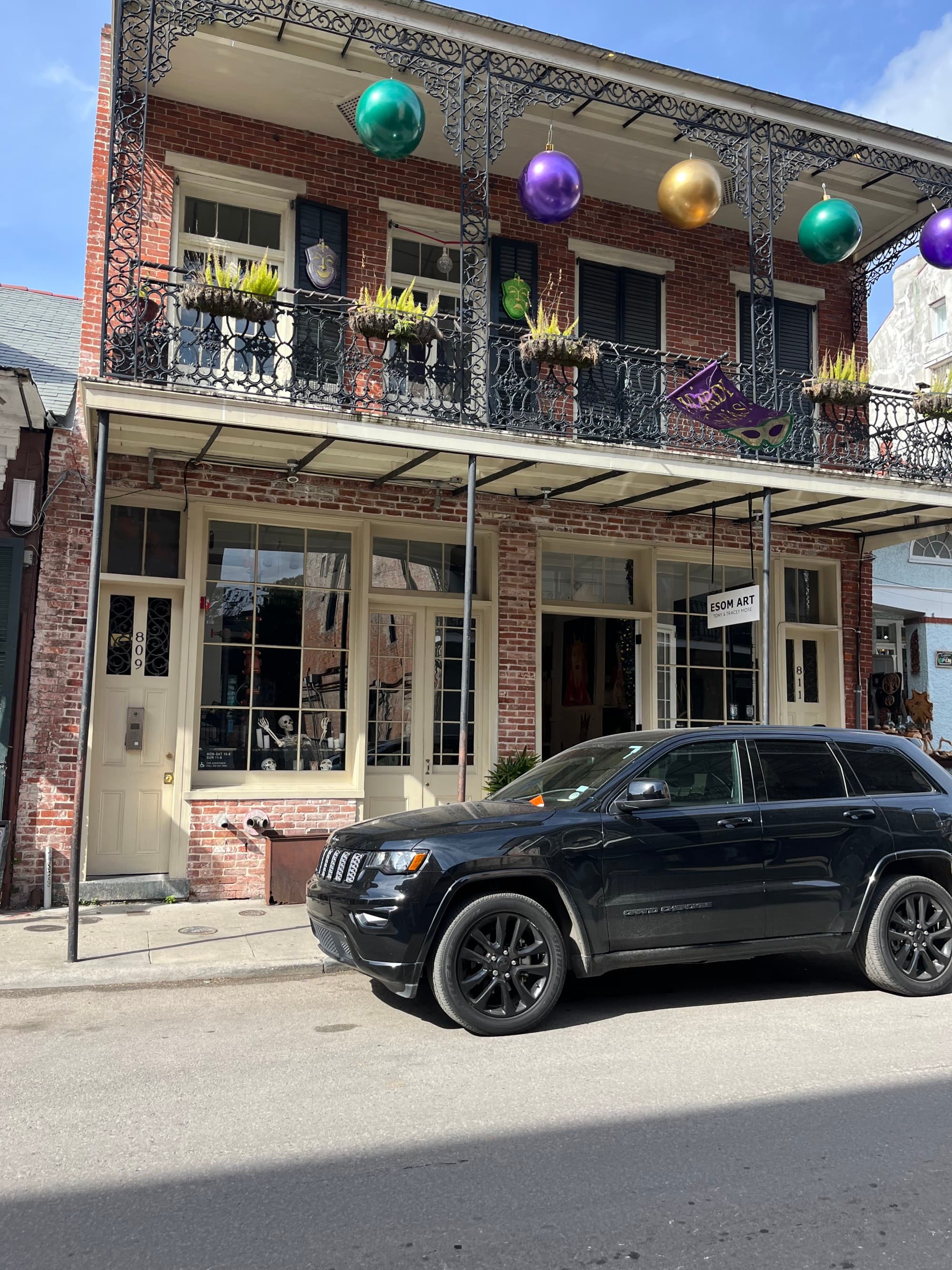 A two-story building with large purple, green and gold baubles hanging from the eaves and a car parked in front.