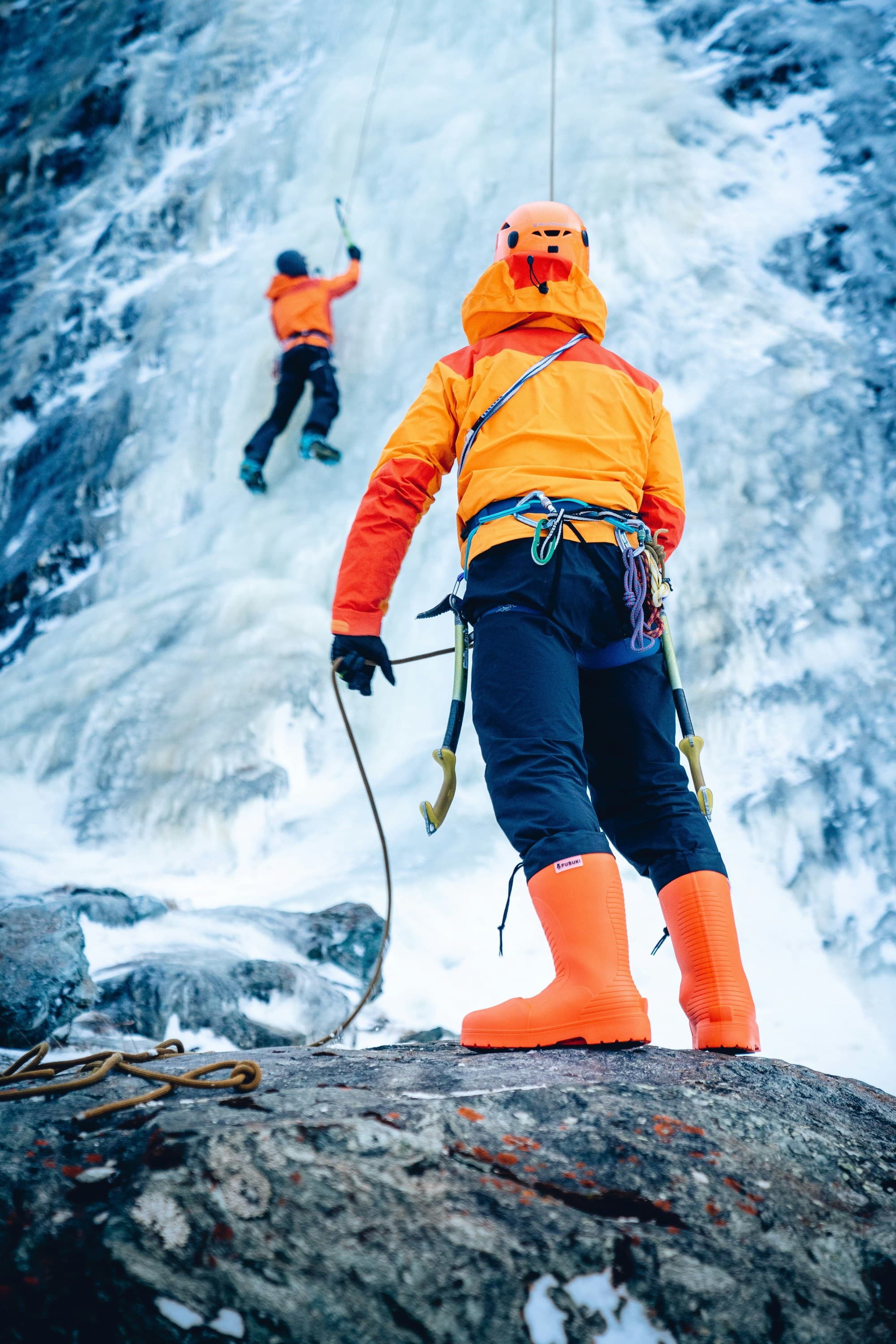 Two people ascending an icy mountain, with ropes, gear and orange outfits.