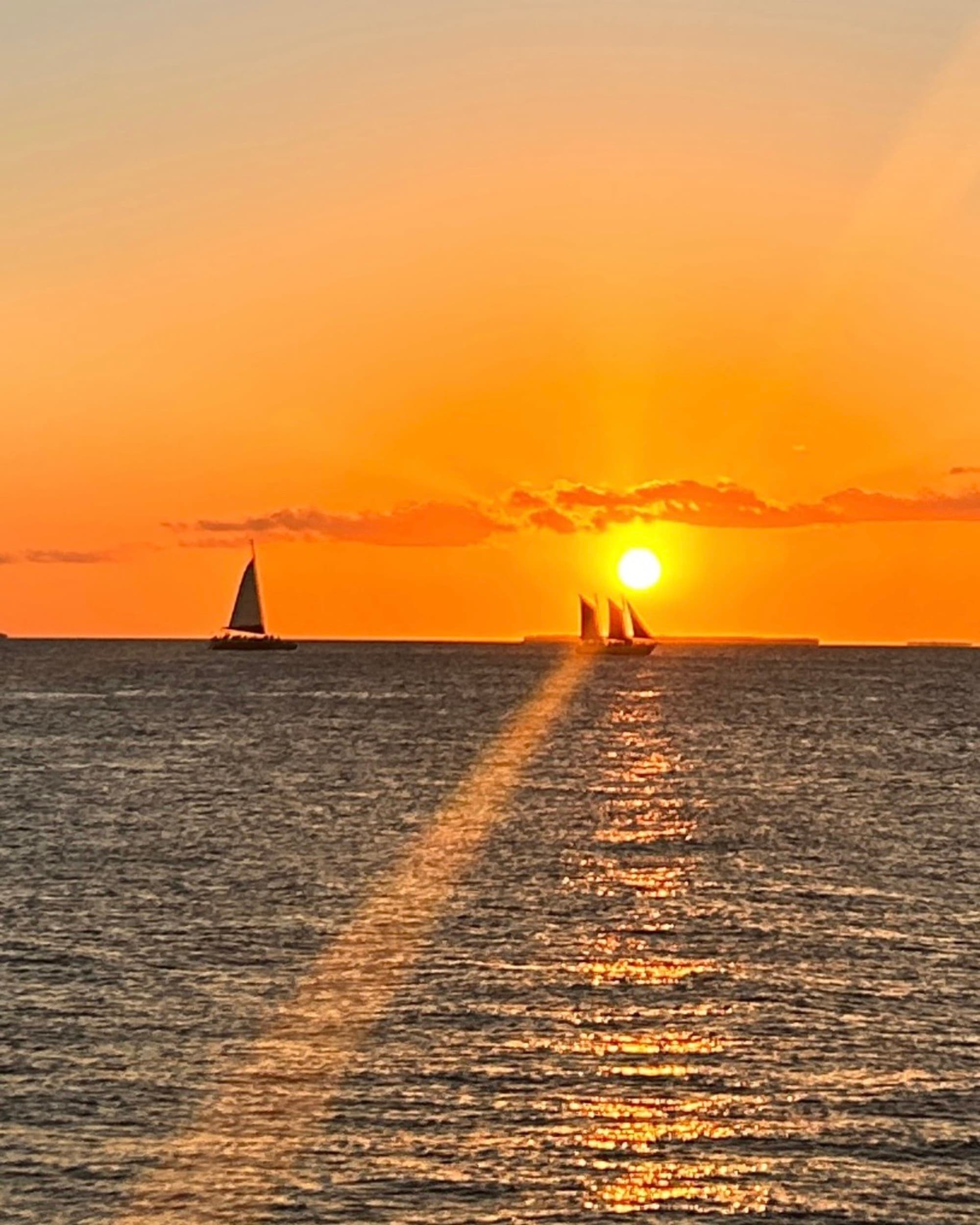 The image portrays a serene sunset over the ocean, with sailboat silhouettes against a vibrant orange sky.