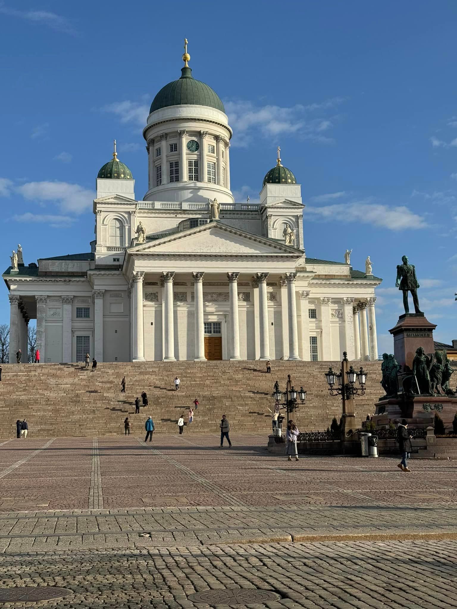 A white building at the top of steps with green domes.