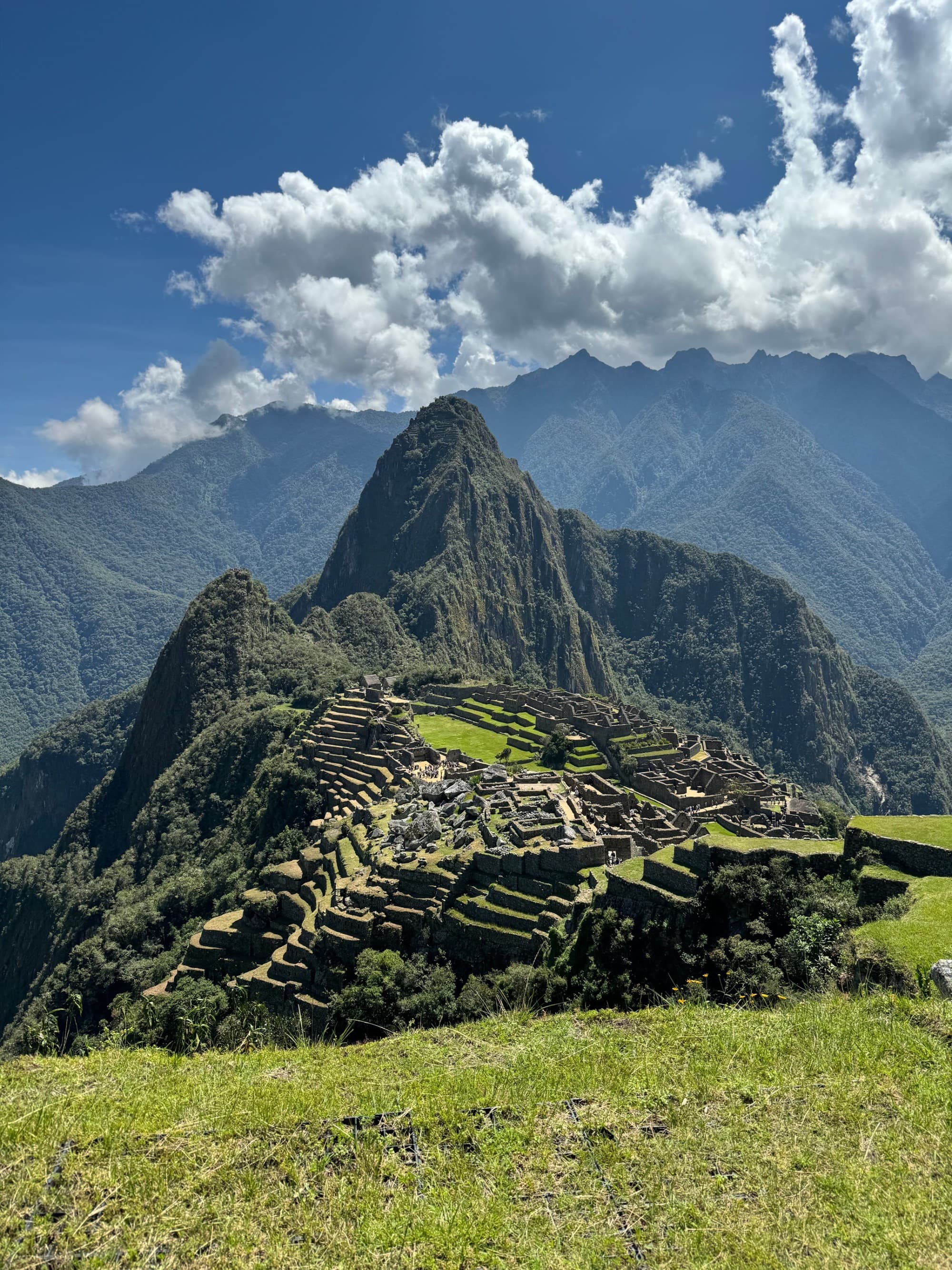 A distant view of Machu Picchu on a sunny day, with mountain ranges and peaks in the distance.