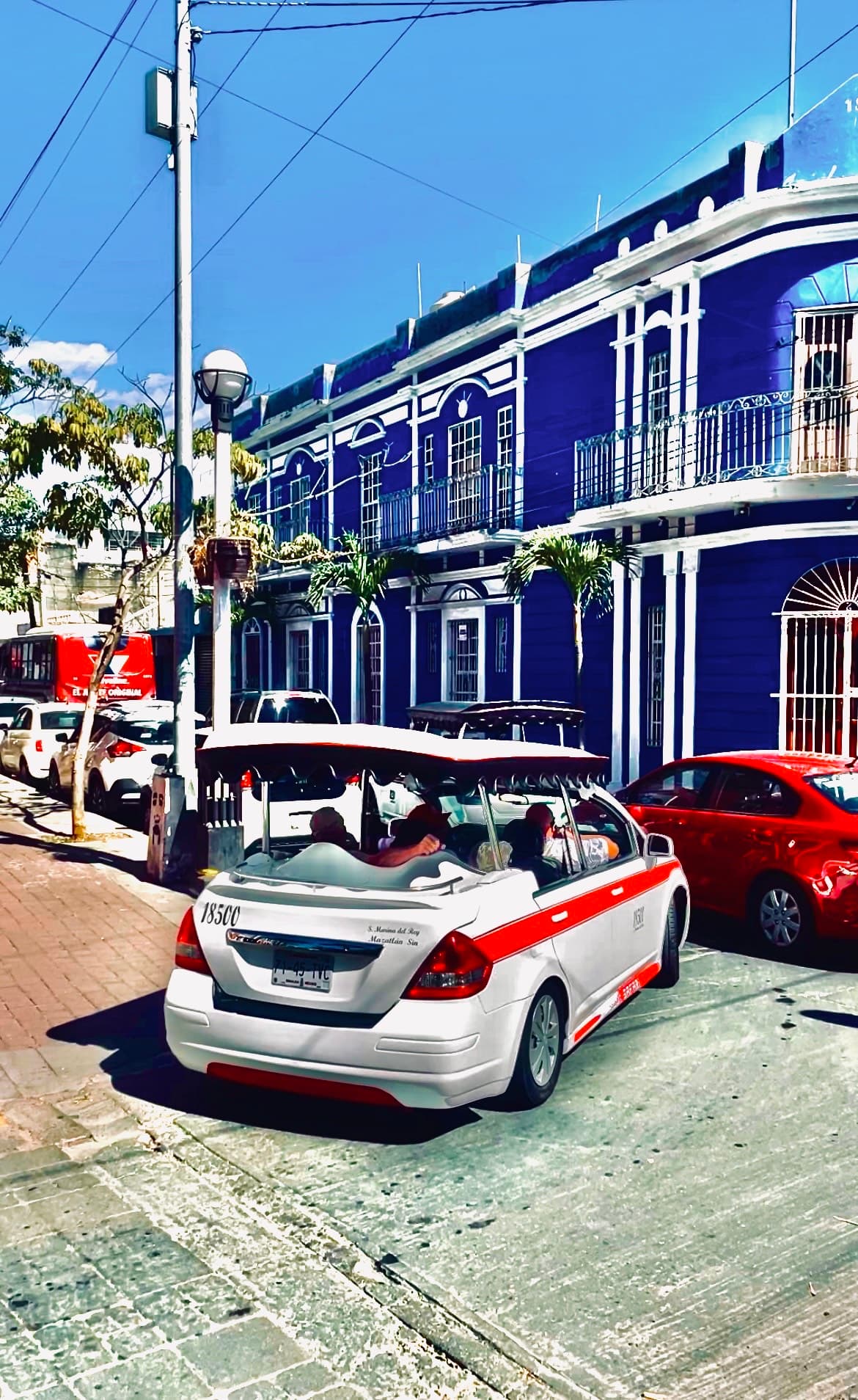 An air taxi and other cars in front of a blue building on a sunny day.