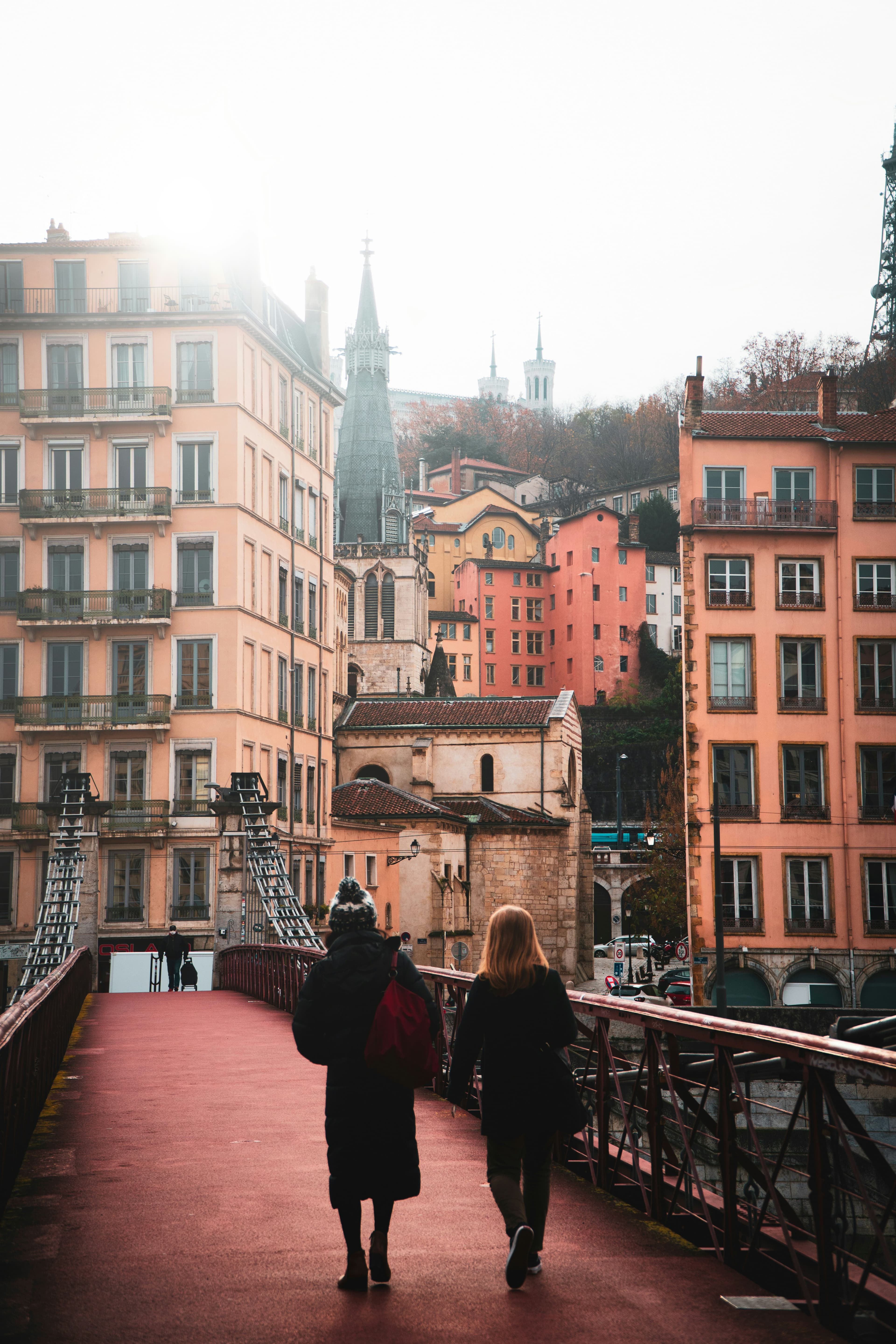 People walking on a bridge in France with city buildings in the distance