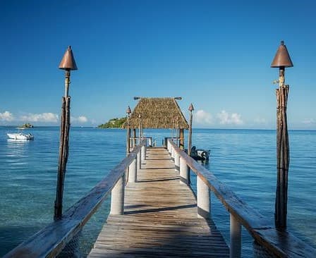 A beautiful of the ocean on a sunny day with a wooden jetty lined with tiki torches.