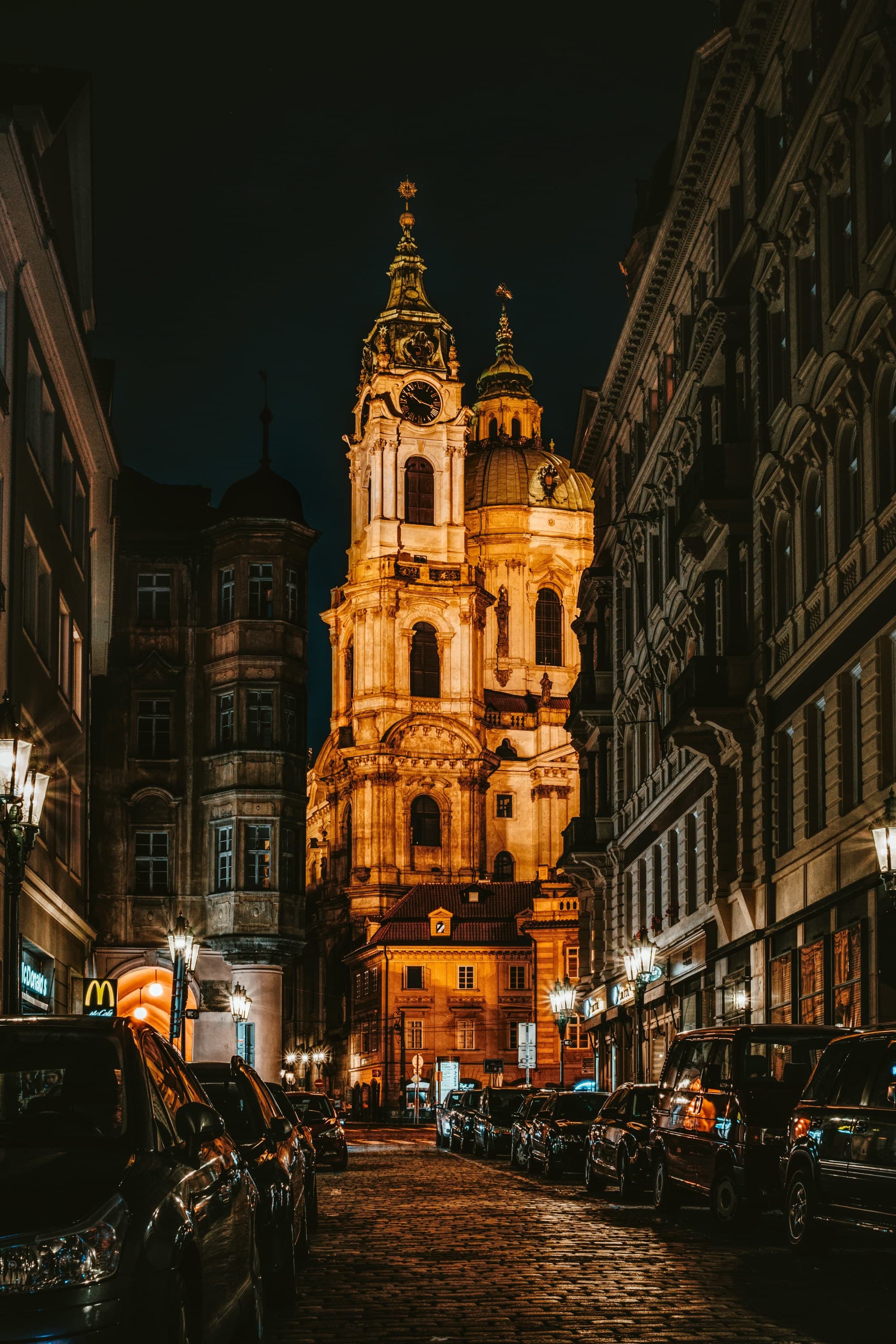 The image depicts a grand, illuminated church at night, creating a striking contrast with the dark, urban surroundings.