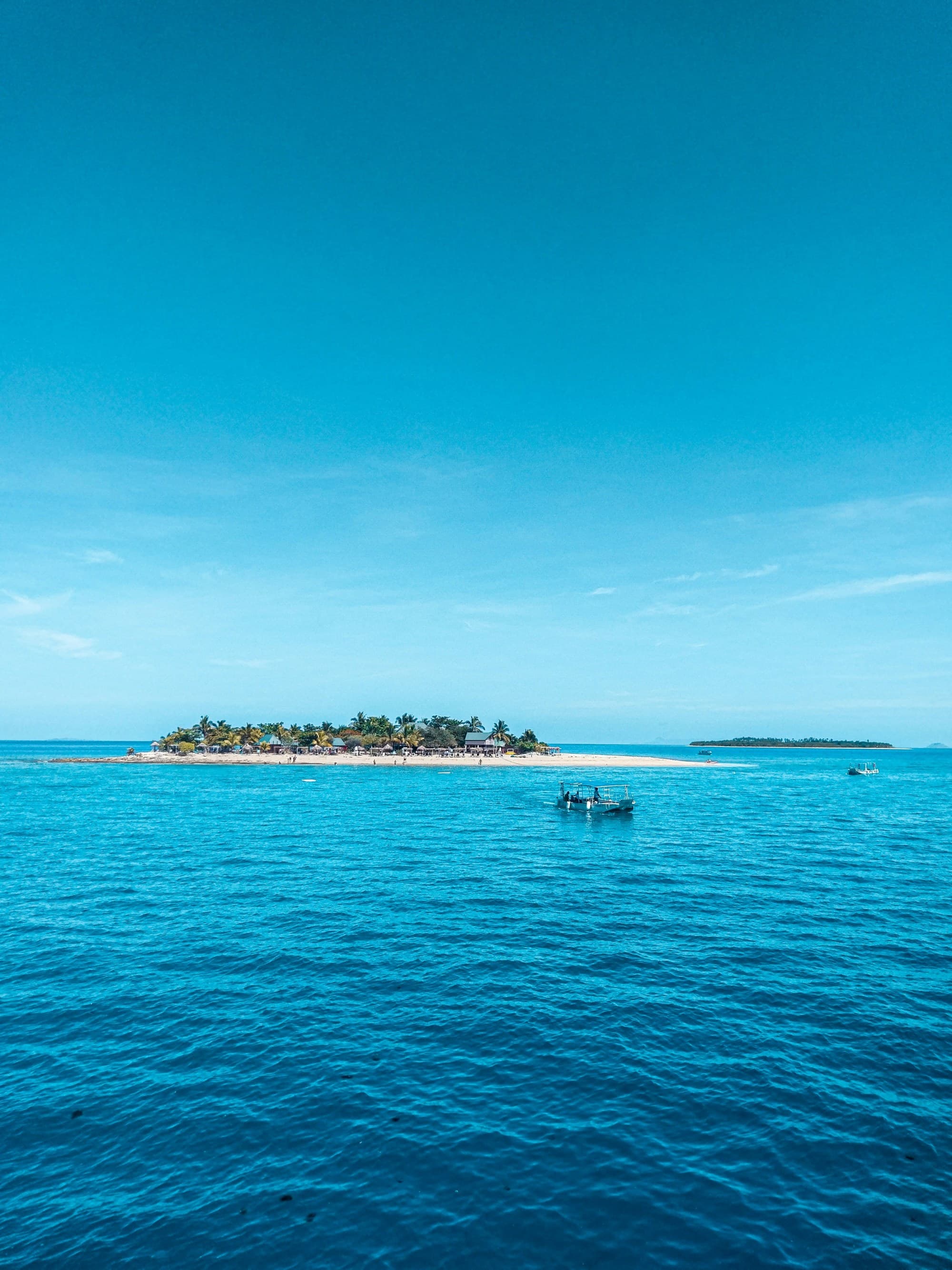 A tranquil tropical seascape with a boat on the water and an island in the distance, under a clear blue sky.