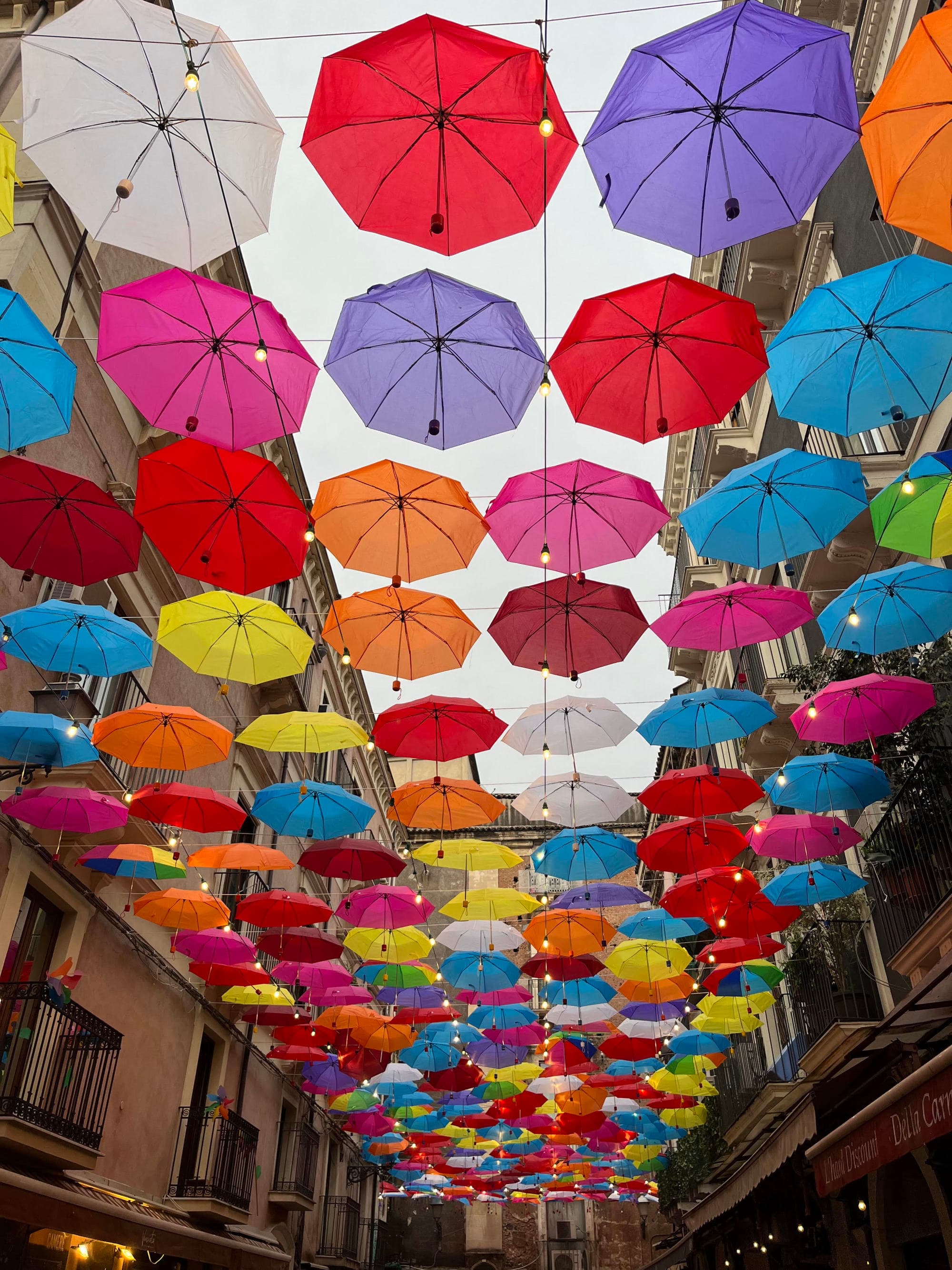 The image displays a vibrant array of colorful umbrellas suspended above a street, creating a festive overhead canopy.