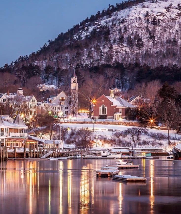 A lake area with snow covered mountains and a cabin in the distance at dusk with nice lighting