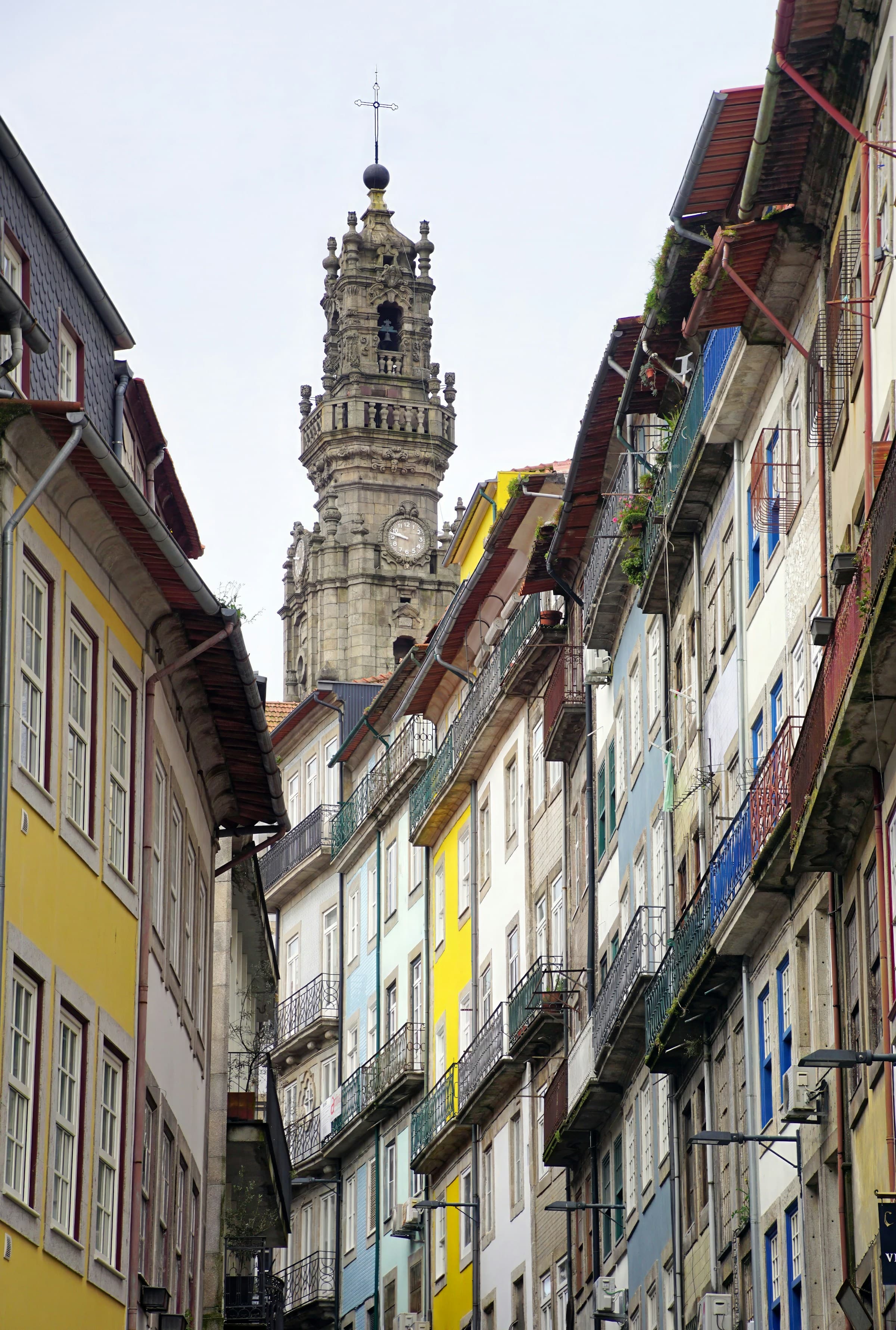 Old buildings on a narrow street with a bell tower behind in Portugal.