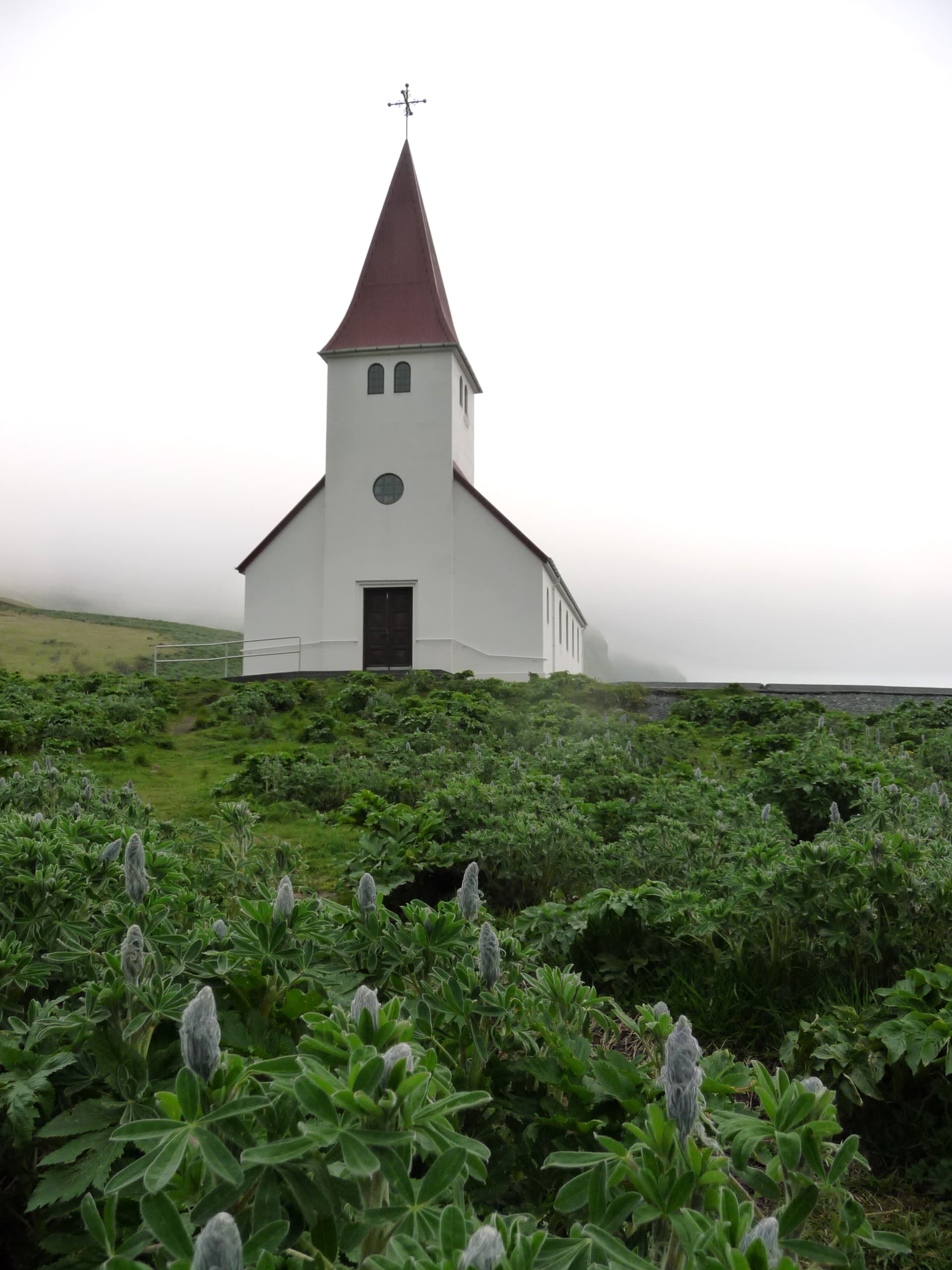 A beautiful view of Reyniskirkja Church resting in an emerald-colored field.