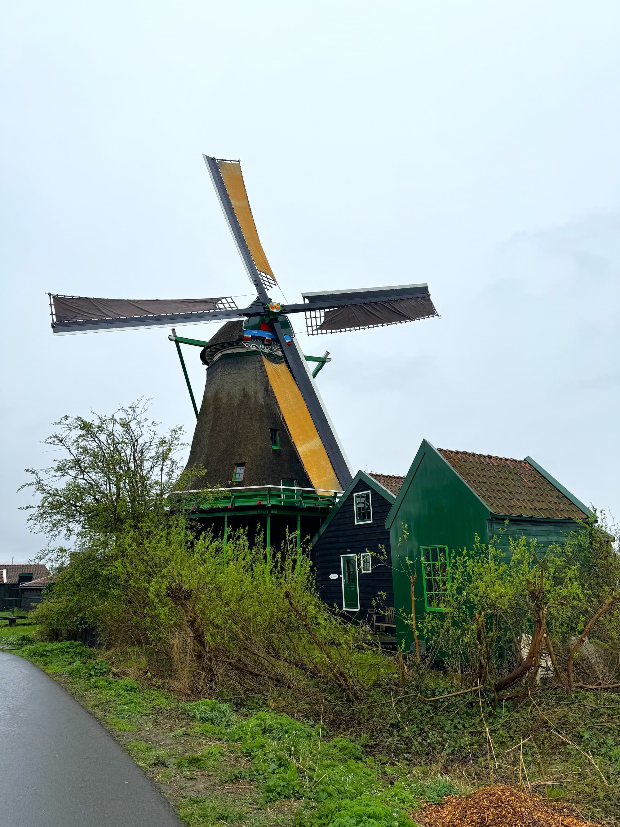 A picturesque countryside scene with a traditional windmill and adjacent green structure under an overcast sky.