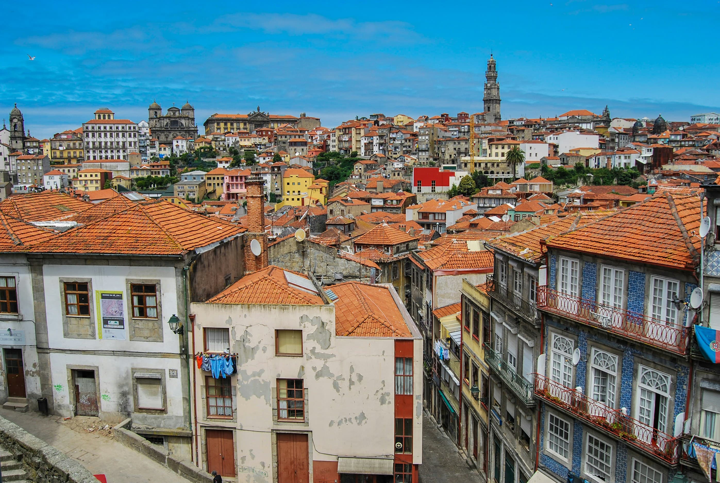 A view of the city of Porto, Portugal, with red rooftops, residential building, and a big, blue sky.