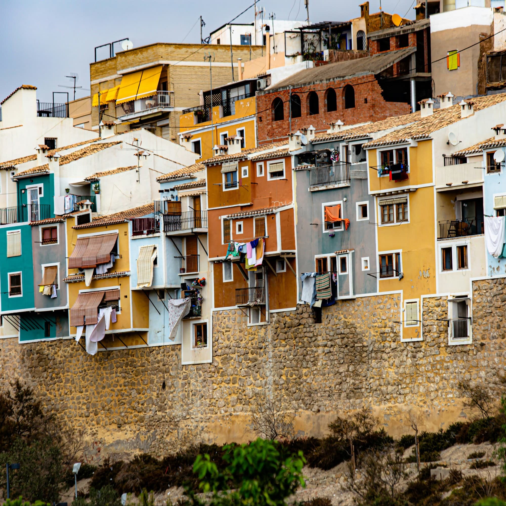 Colorful houses and apartment buildings in rows, above a stone wall in Spain.