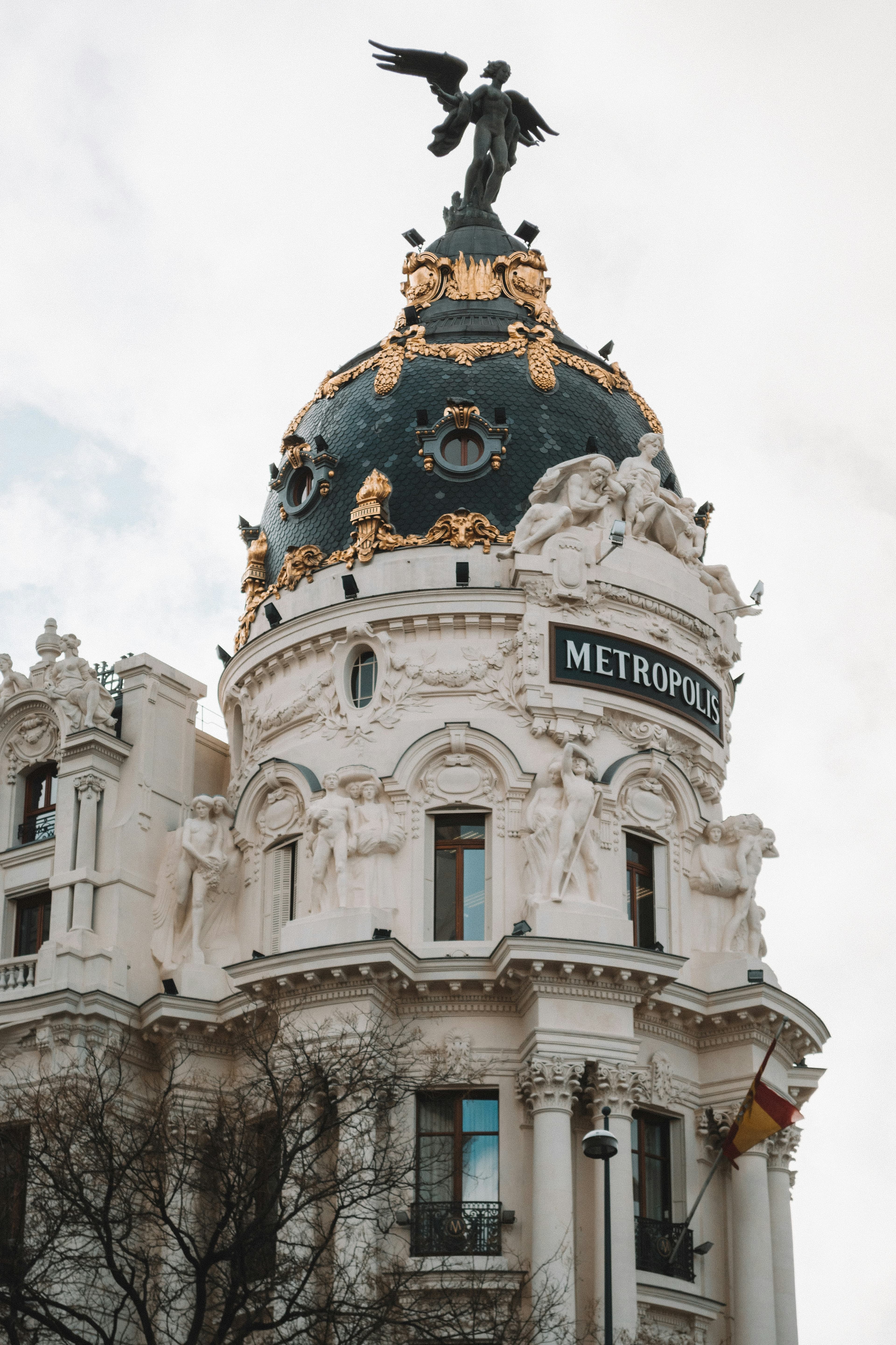 An ornate domed building in Madrid with a black and gold roof and an angel statue on top.