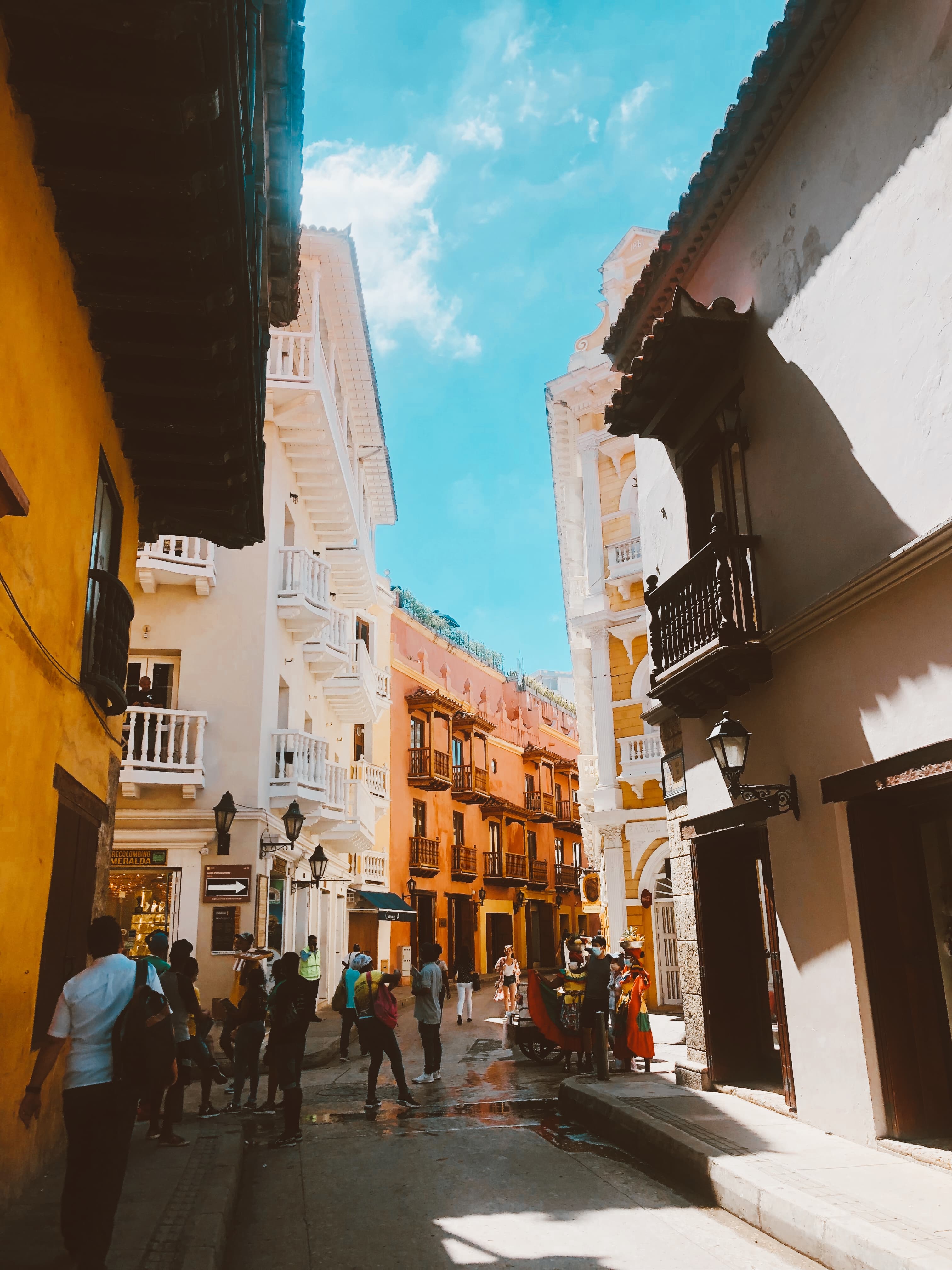 A vibrant street scene of Cartagena's Old Town, with colorful buildings, street vendors in traditional dress and tourists on a sunny day.