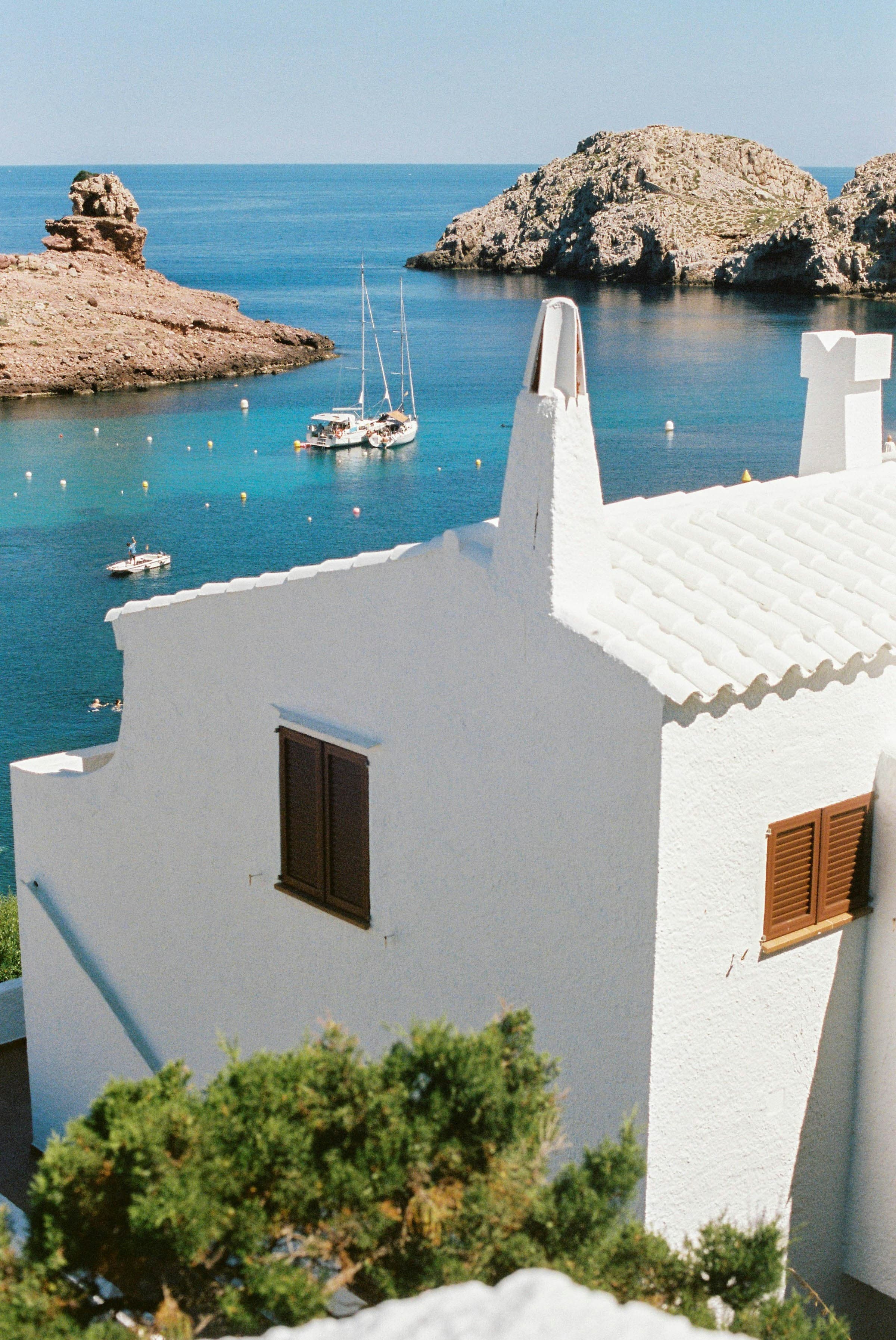 An aerial view of a Mediterranean coastal town, with a view of buildings, mountains, and the azure sea.