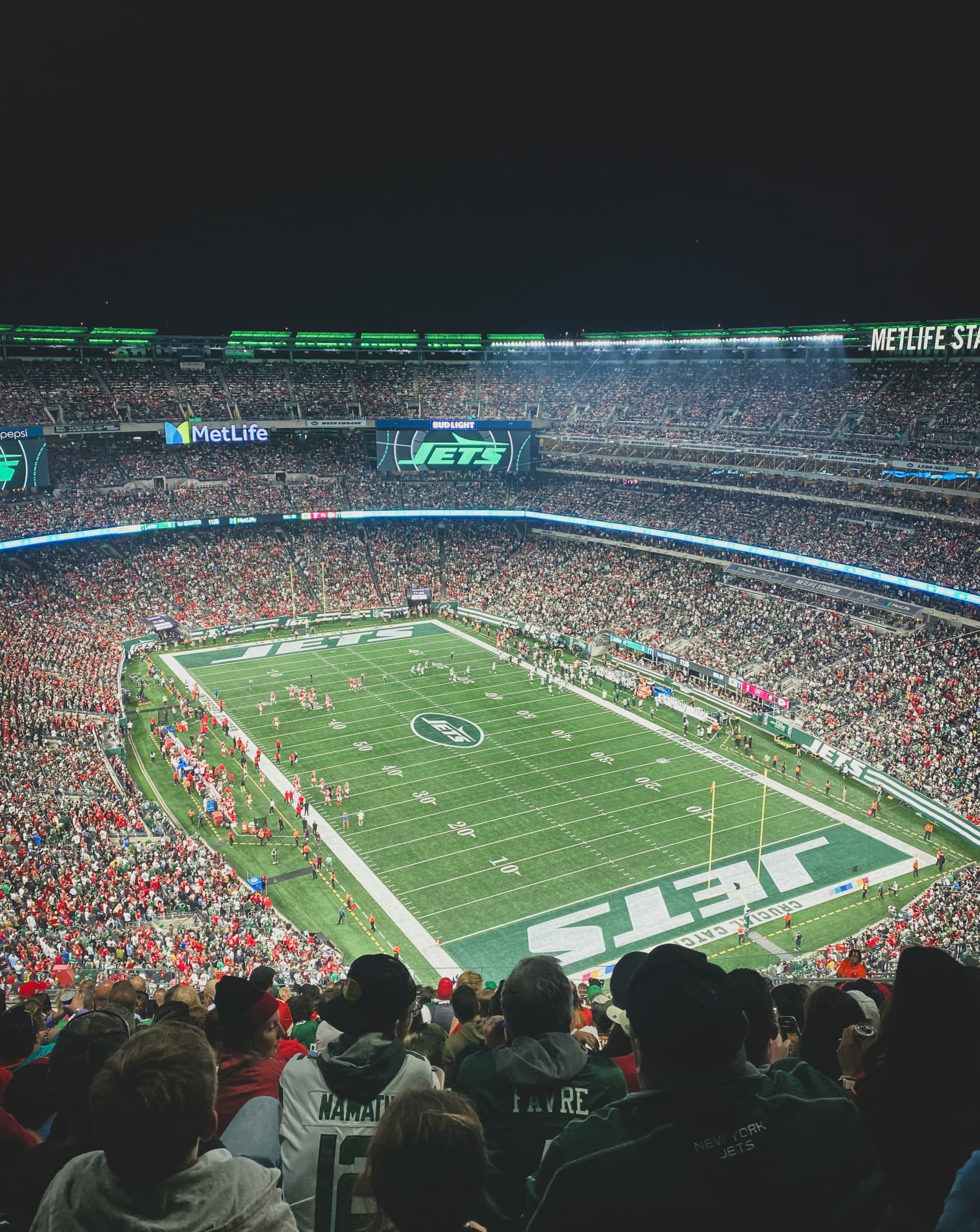 The image presents a lively football stadium teeming with spectators, showcasing the energetic ambiance of a night game from an aerial perspective.