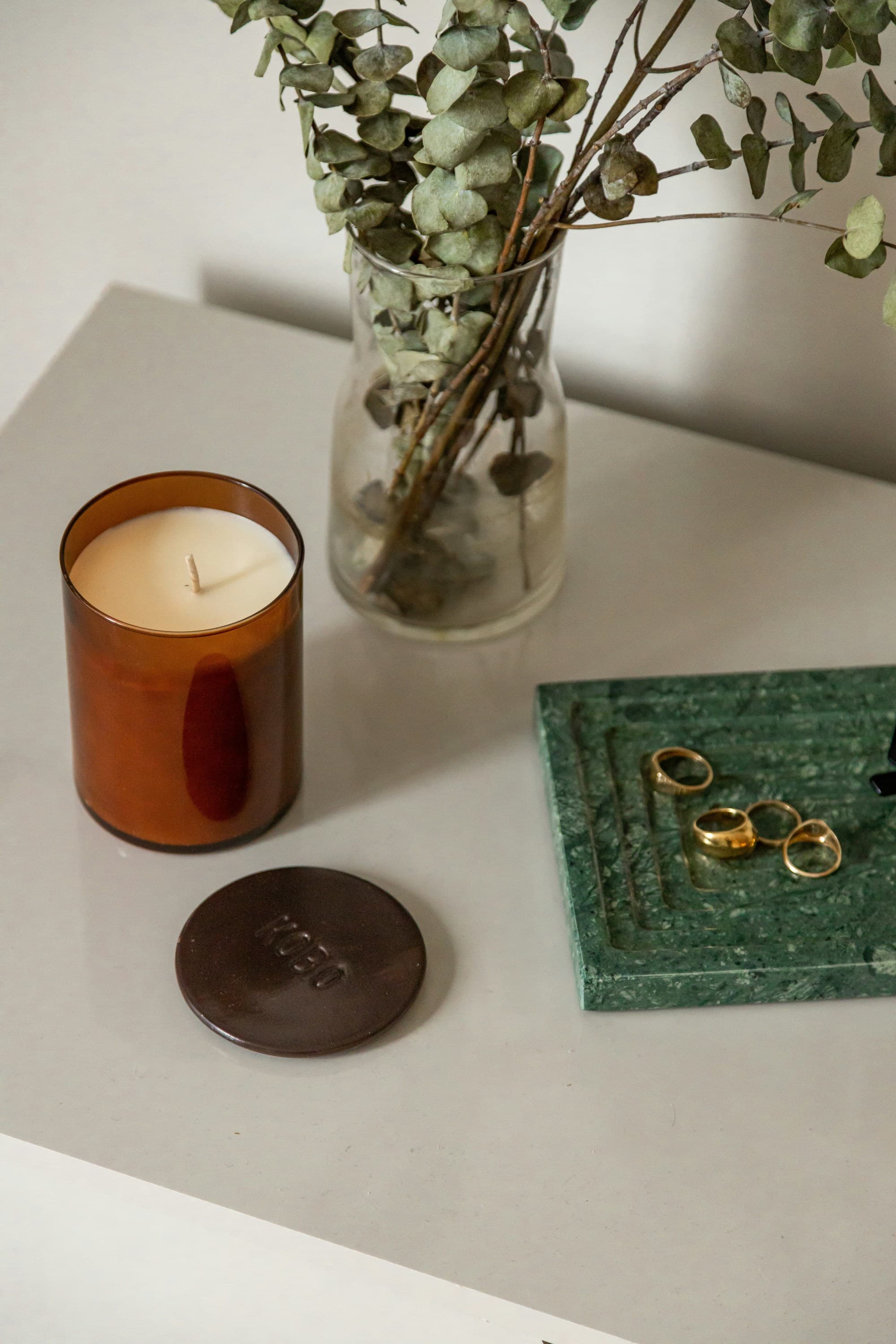 The image presents a still-life arrangement with a candle, eucalyptus branches, and a green book with rings on a light surface at a spa in Aspen.