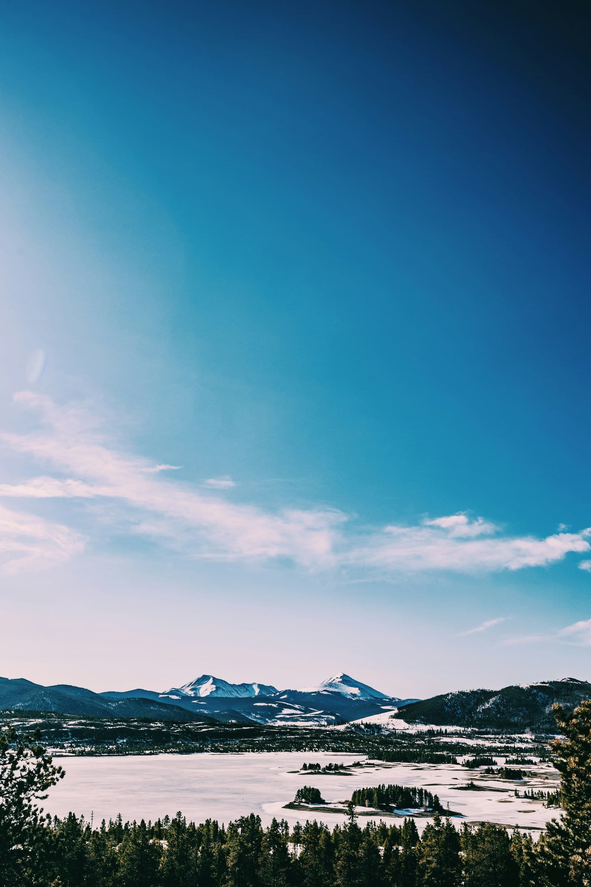 A serene snowy landscape with distant mountains under a clear blue sky, bathed in bright sunlight, in Aspen in winter.