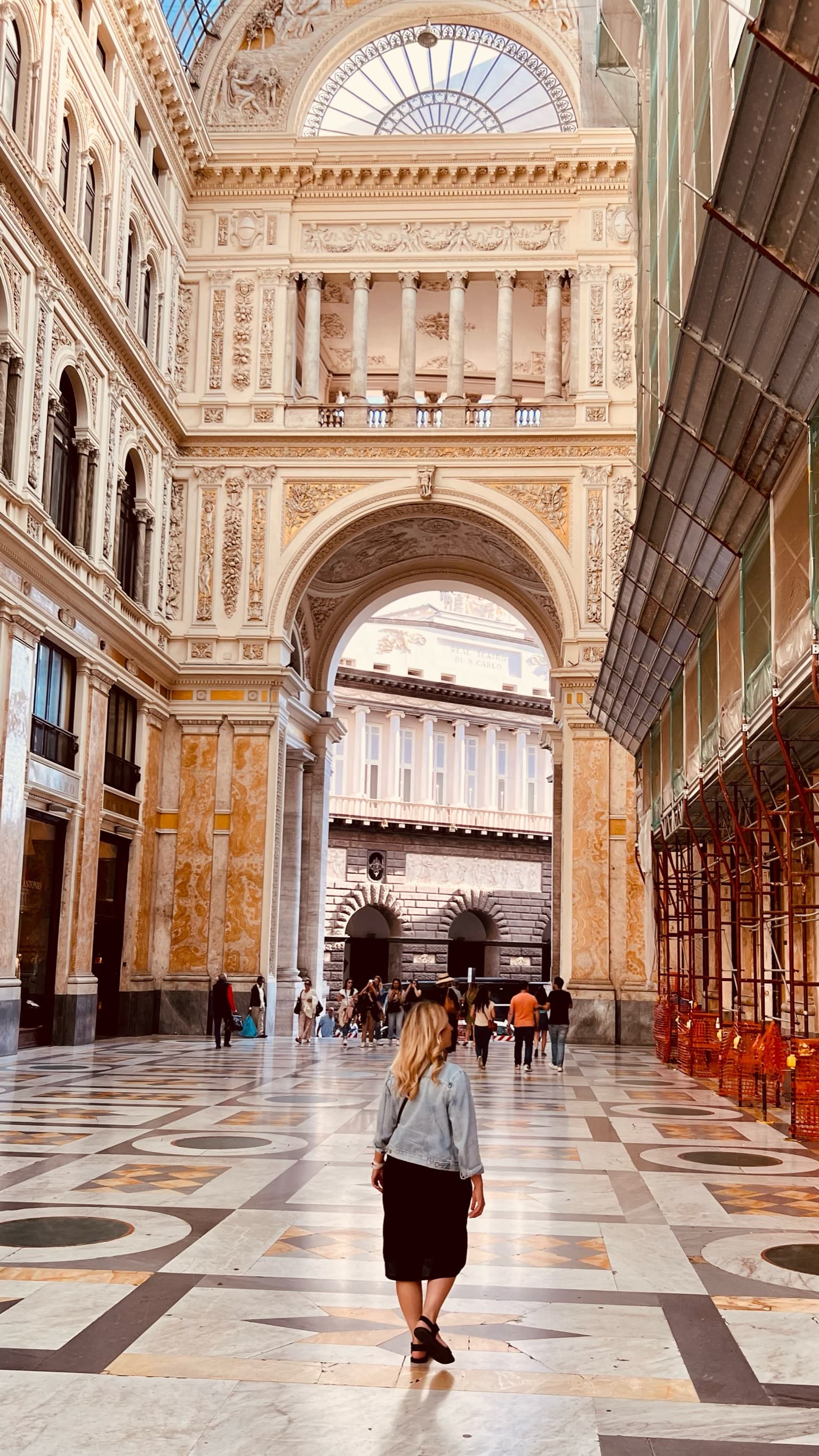 A woman standing inside of a grand building, with an archway leading outside in the background.