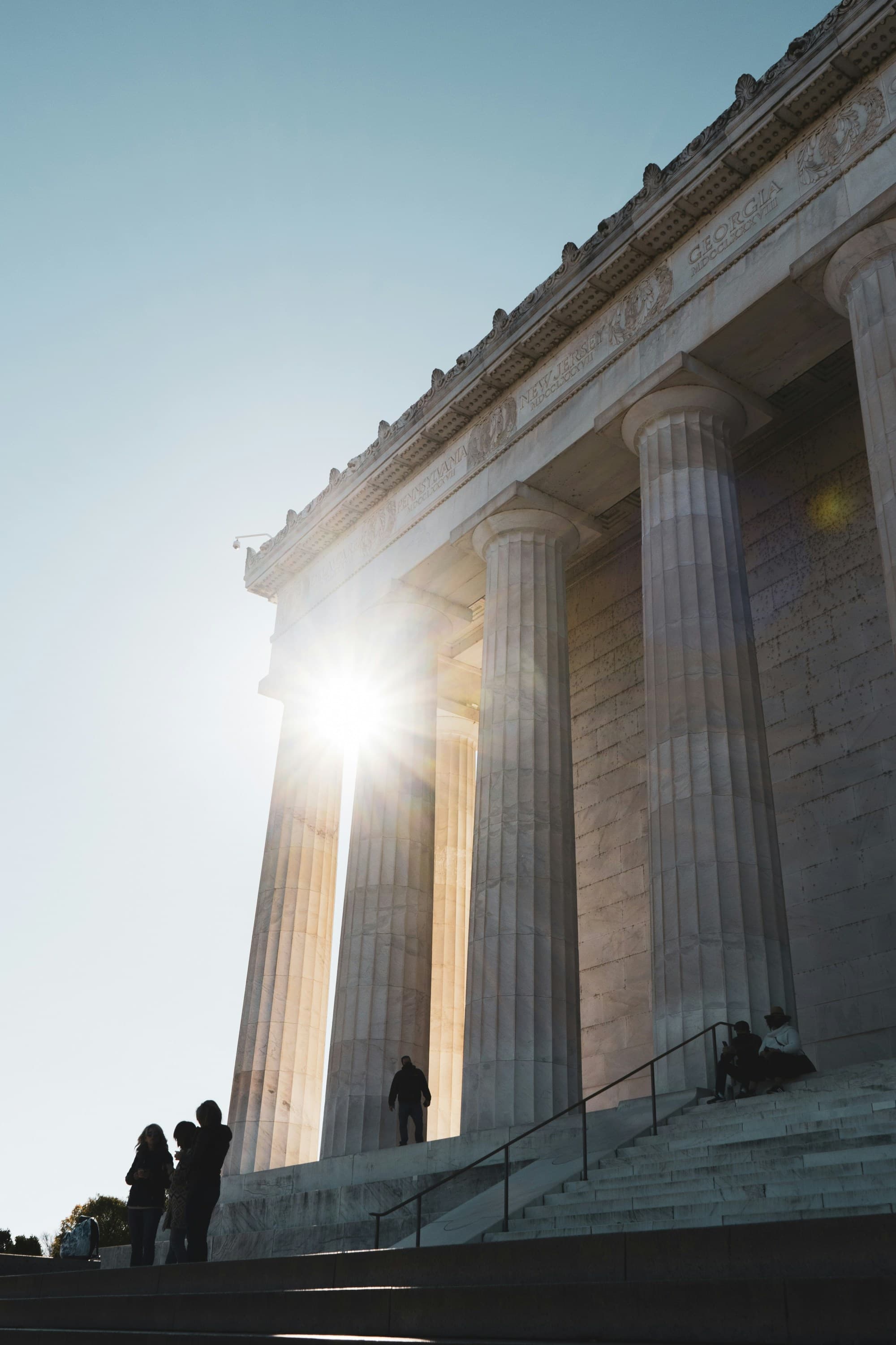 A picture of a white concrete building with pillars in front of it during daytime.