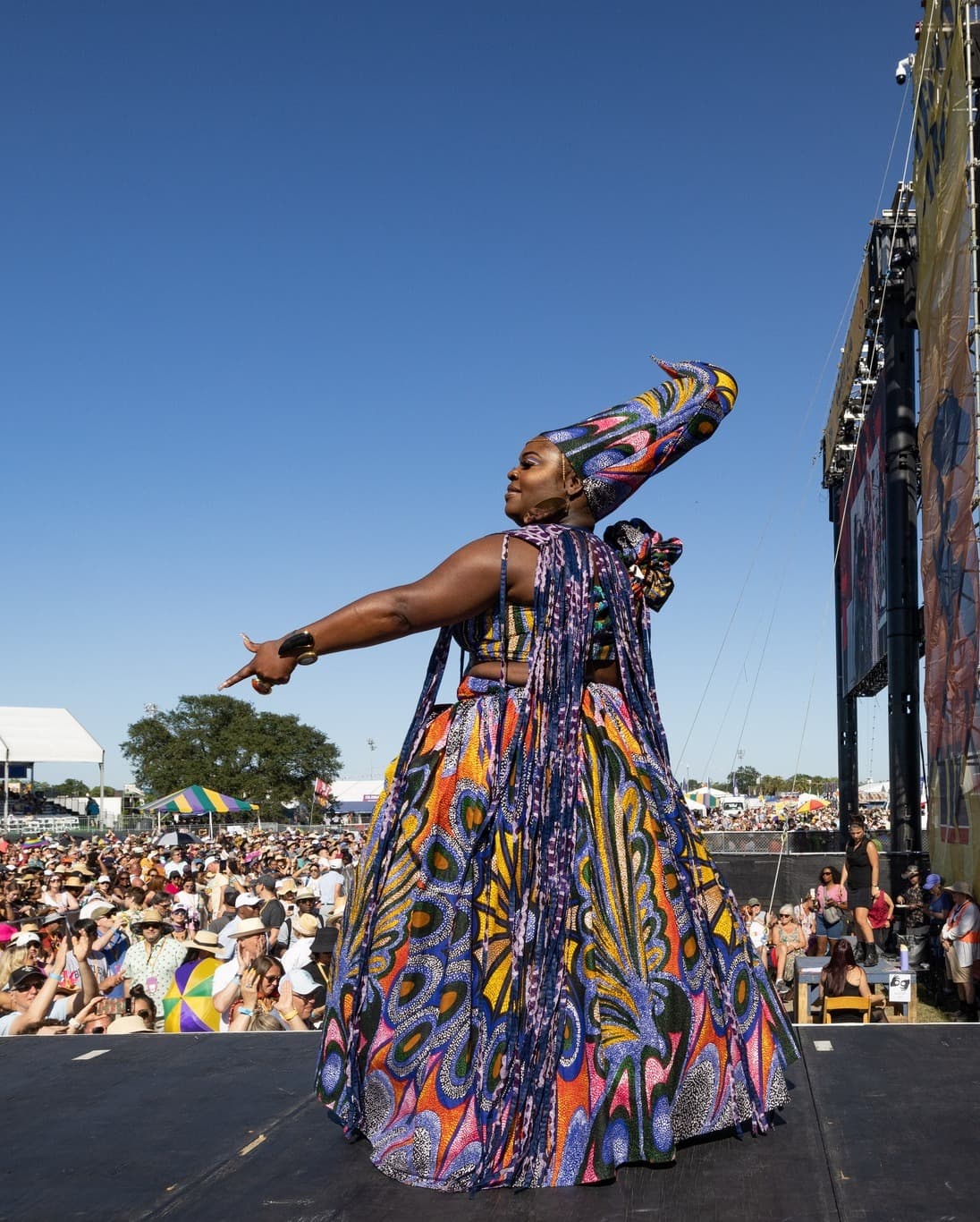 An artist in a colorful outfit and headpiece on stage performing at the New Orleans Jazz & Heritage Festival, one of the New Orleans festivals in 2024.