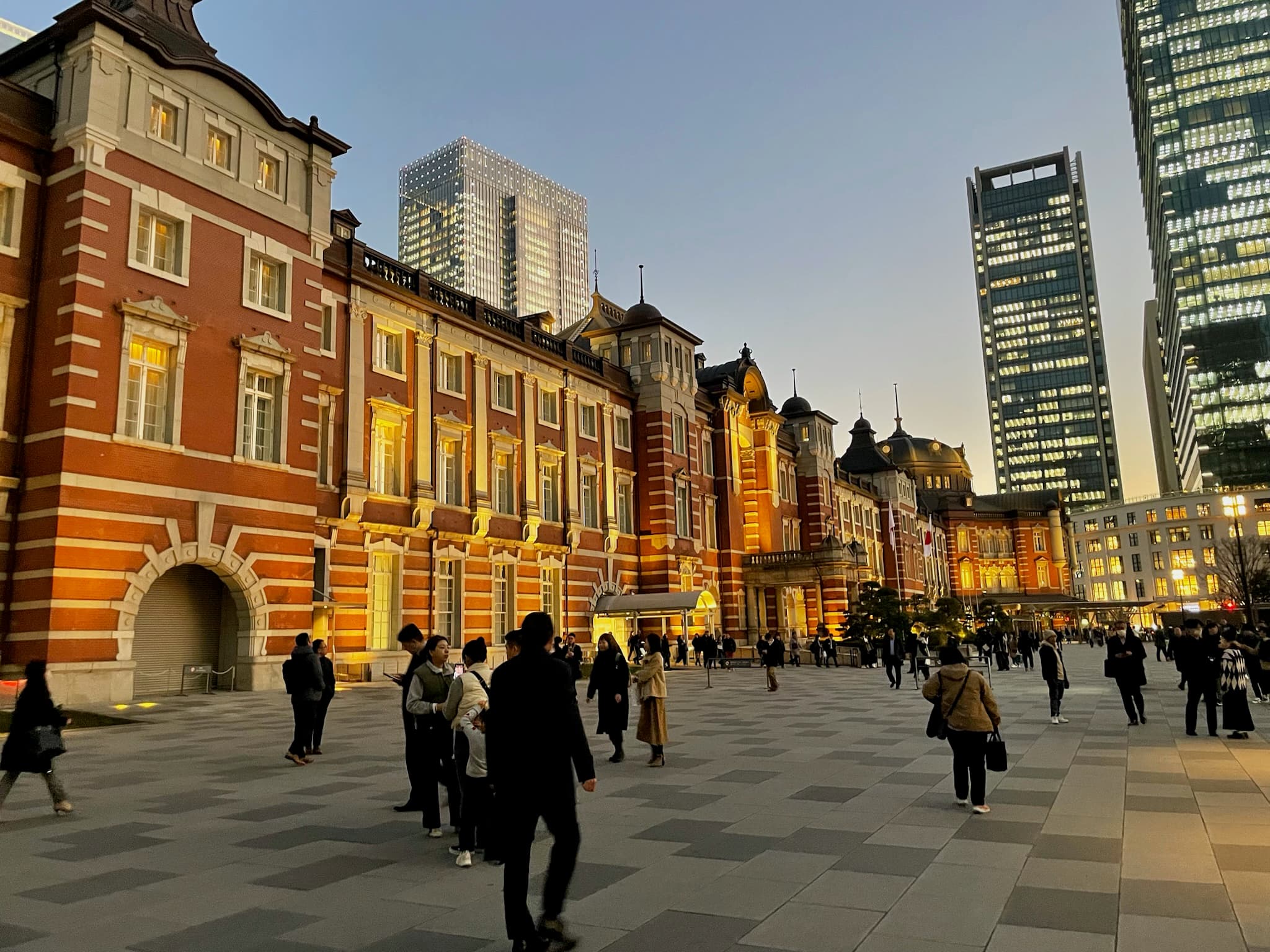 A photo taken during travel to Tokyo near red brick buildings in the evening light with people walking and some skyscrapers in view