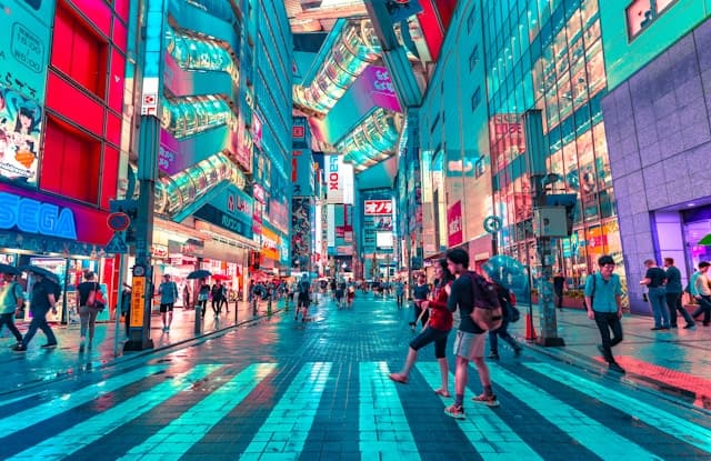 people walking on road near skyscrapers covered in neon billboards.