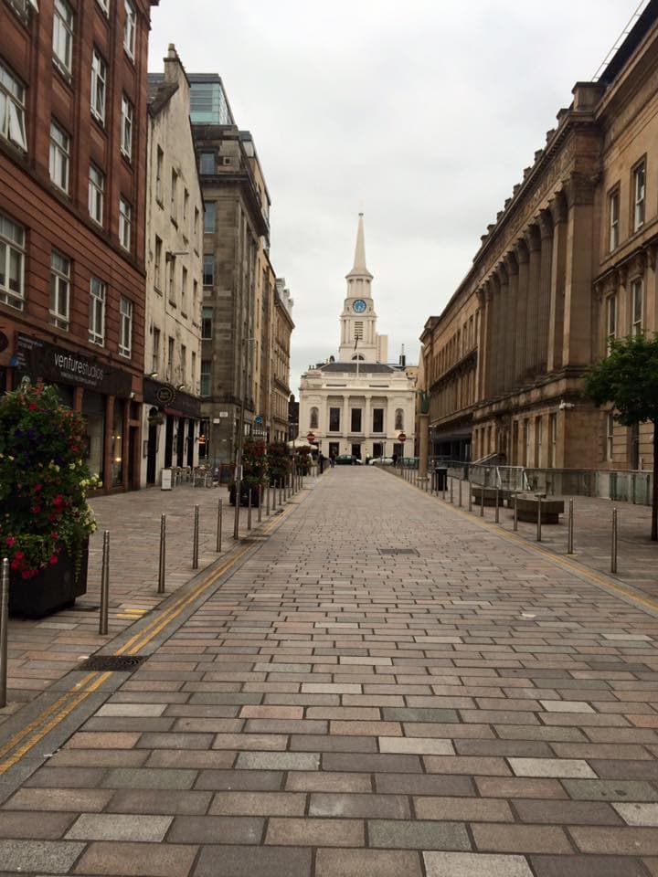 A European city street leading to a white building with a tower in the distance.