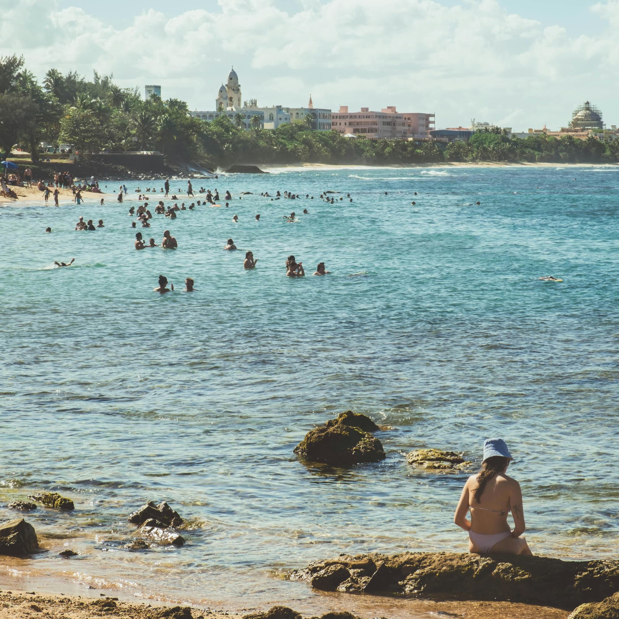 An aerial view of the beach with people swimming in the water during the daytime.