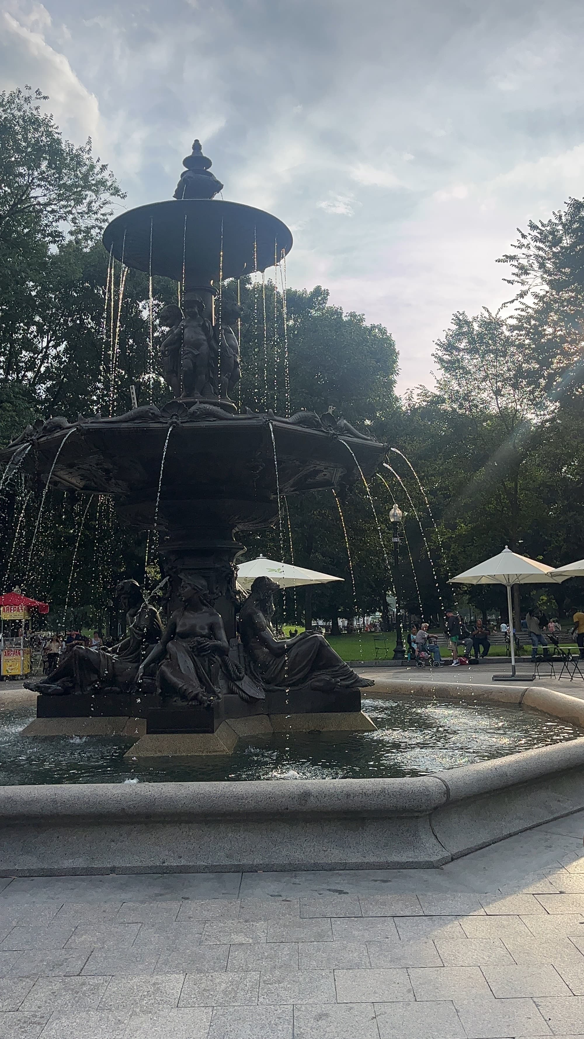 A picture of a black-colored fountain surrounded by trees during the daytime.