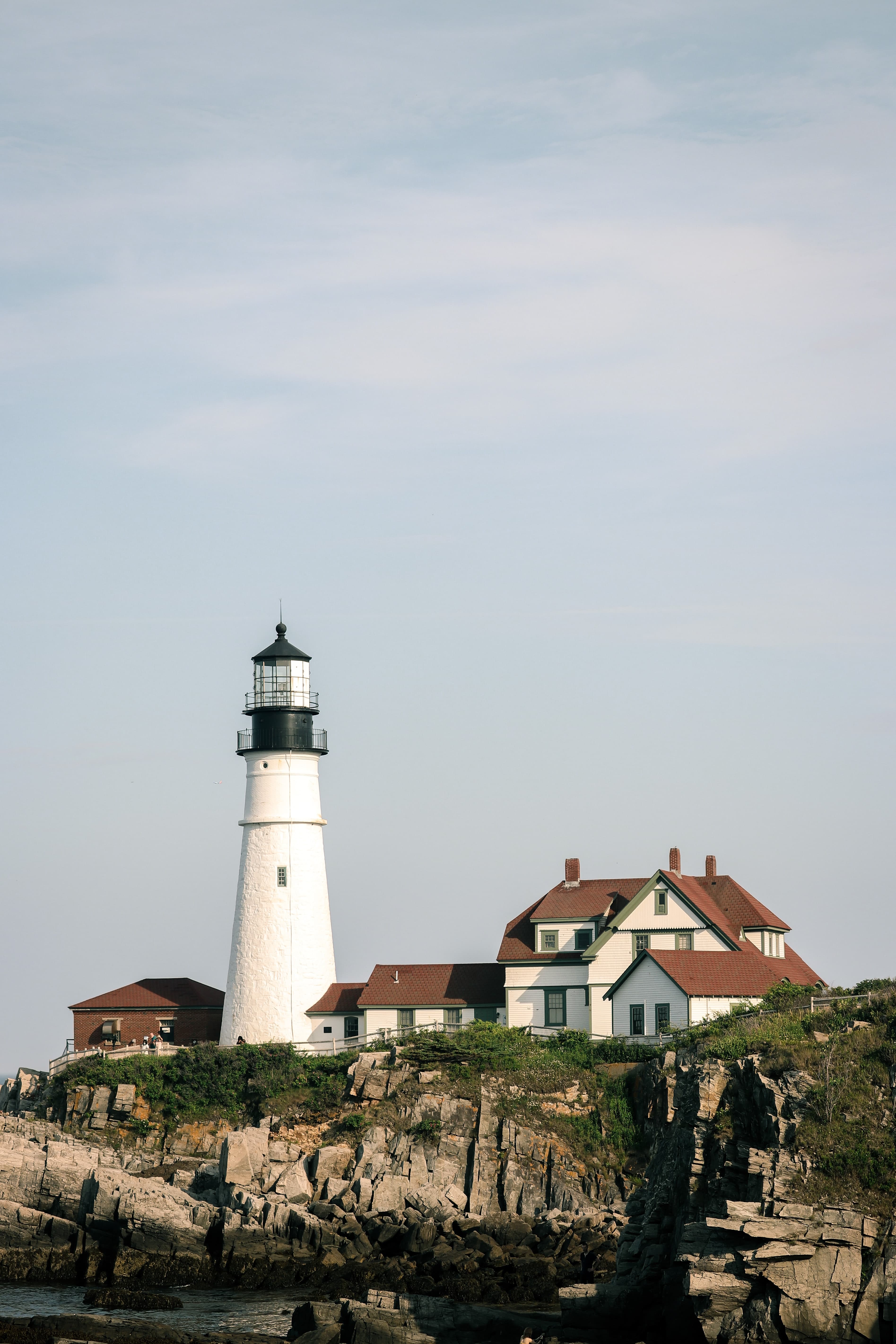 White lighthouse next to house on cliff during daytime