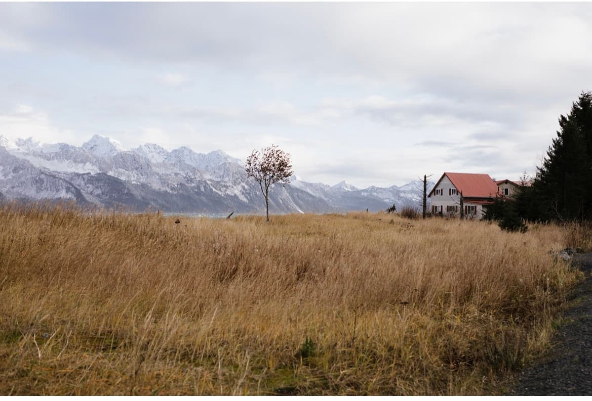 a solitary cabin on a grassy meadow in front of snowy peaks