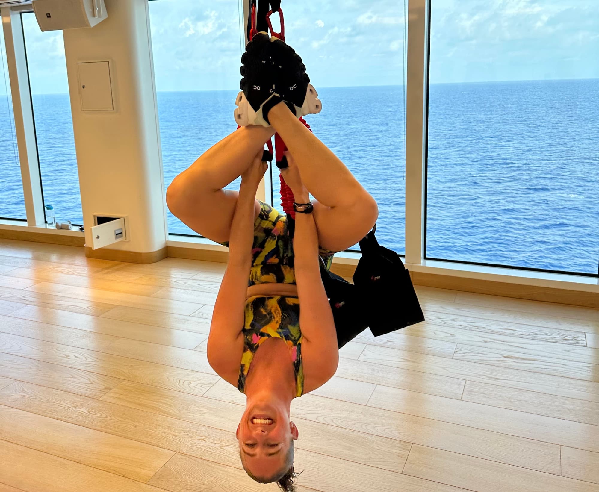 A girl hanging upside down by a rope with blue water in the background.