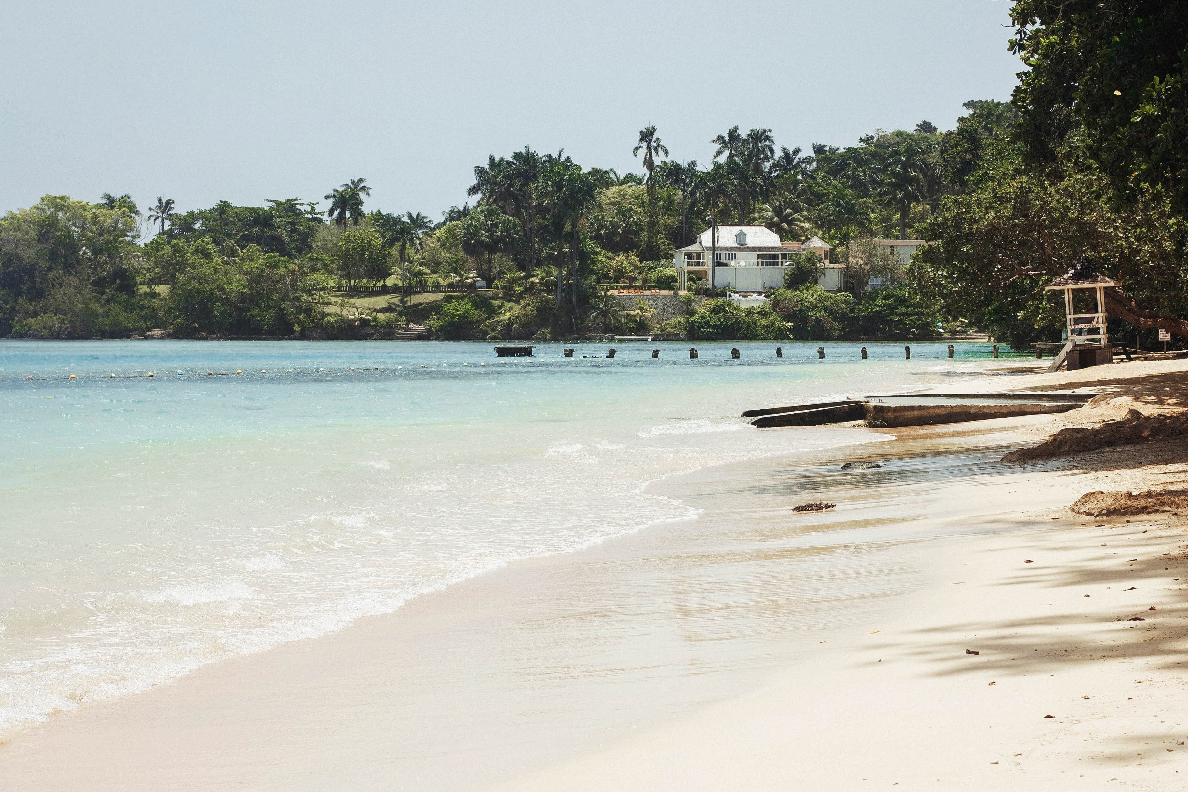 Jamaica island with tan sand and blue water green tall palm trees and a dock with a white house