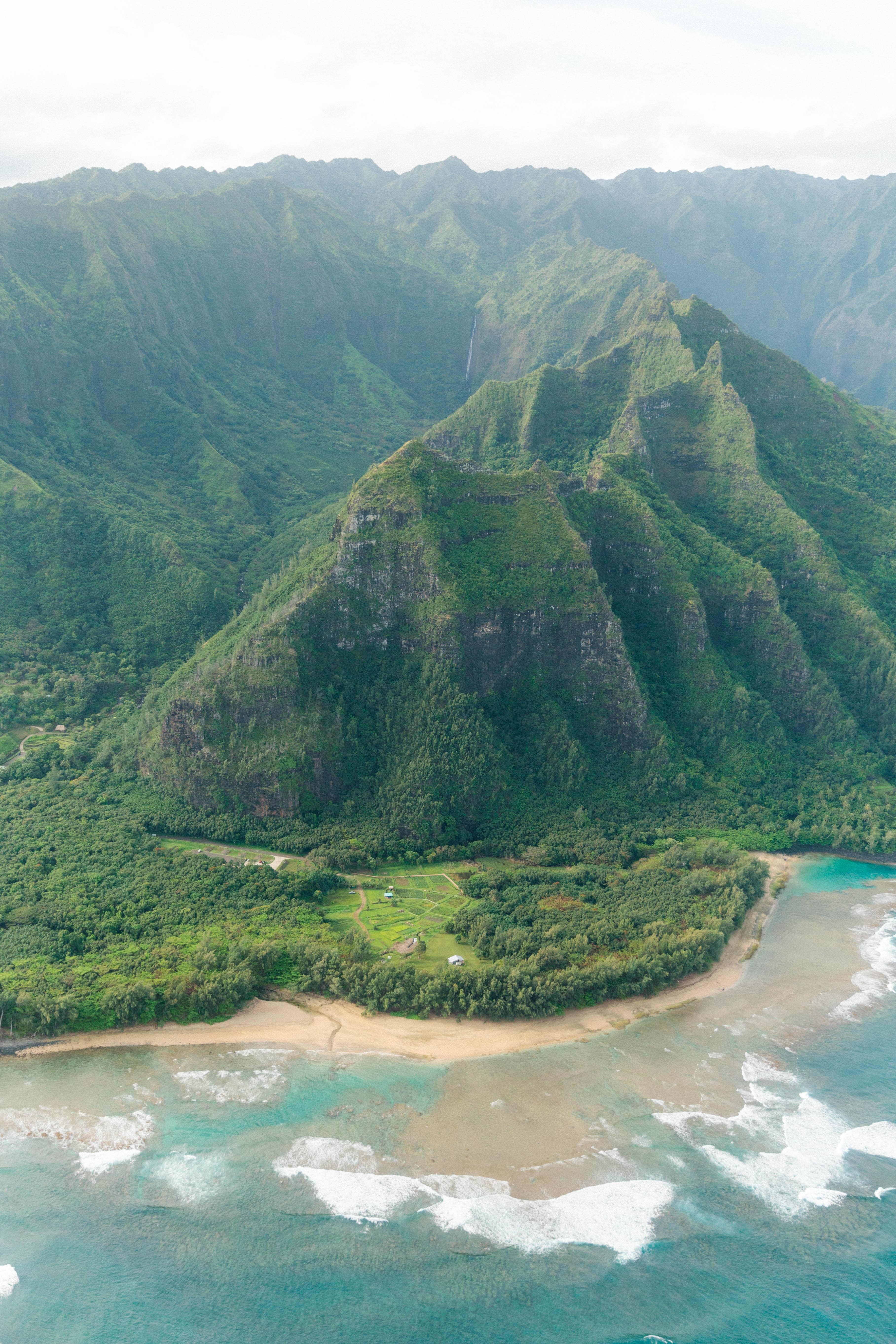 Aerial view of green mountains next to sandy beach and body of water during daytime