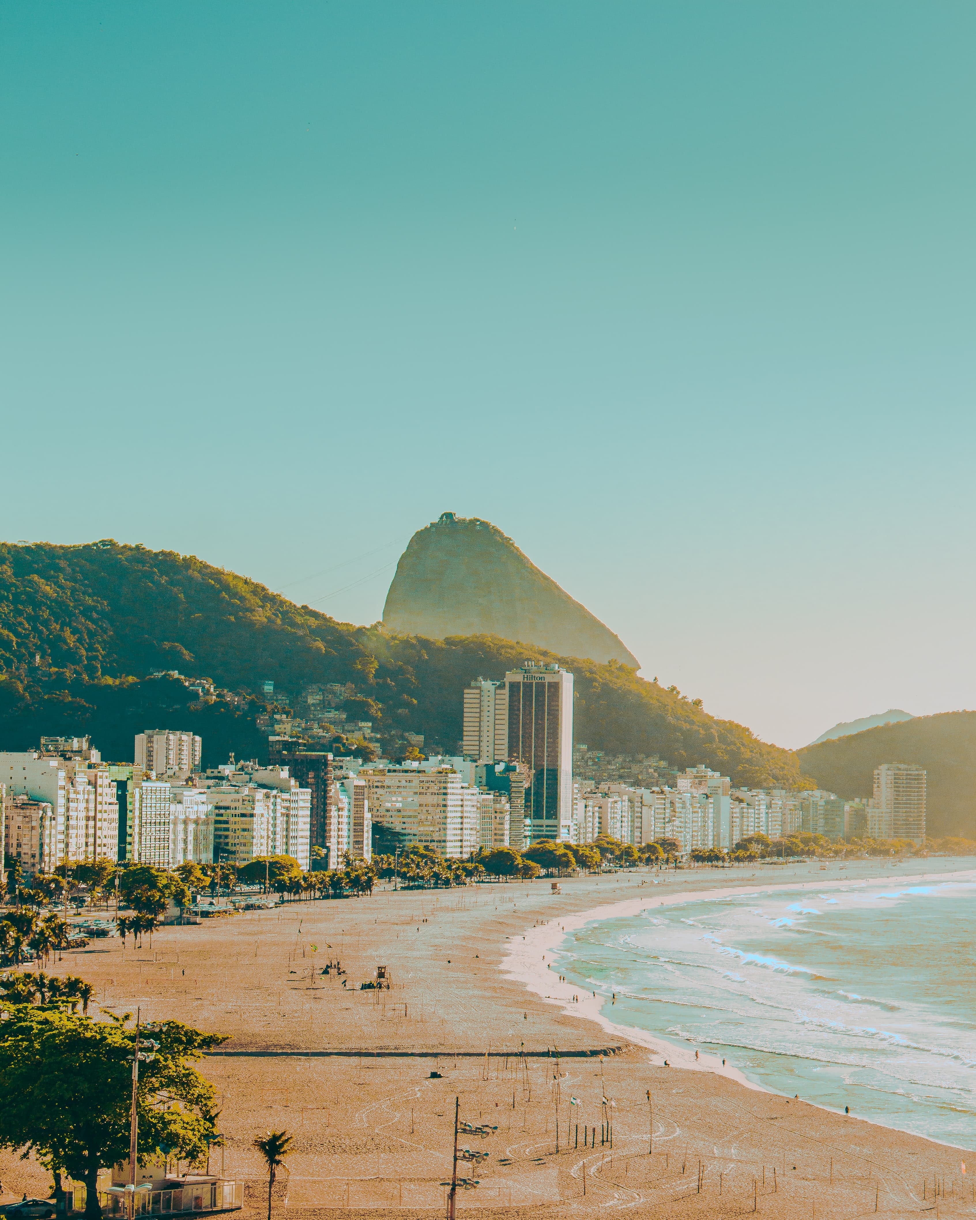 Beach next to ocean with buildings in background with clear skies during daytime