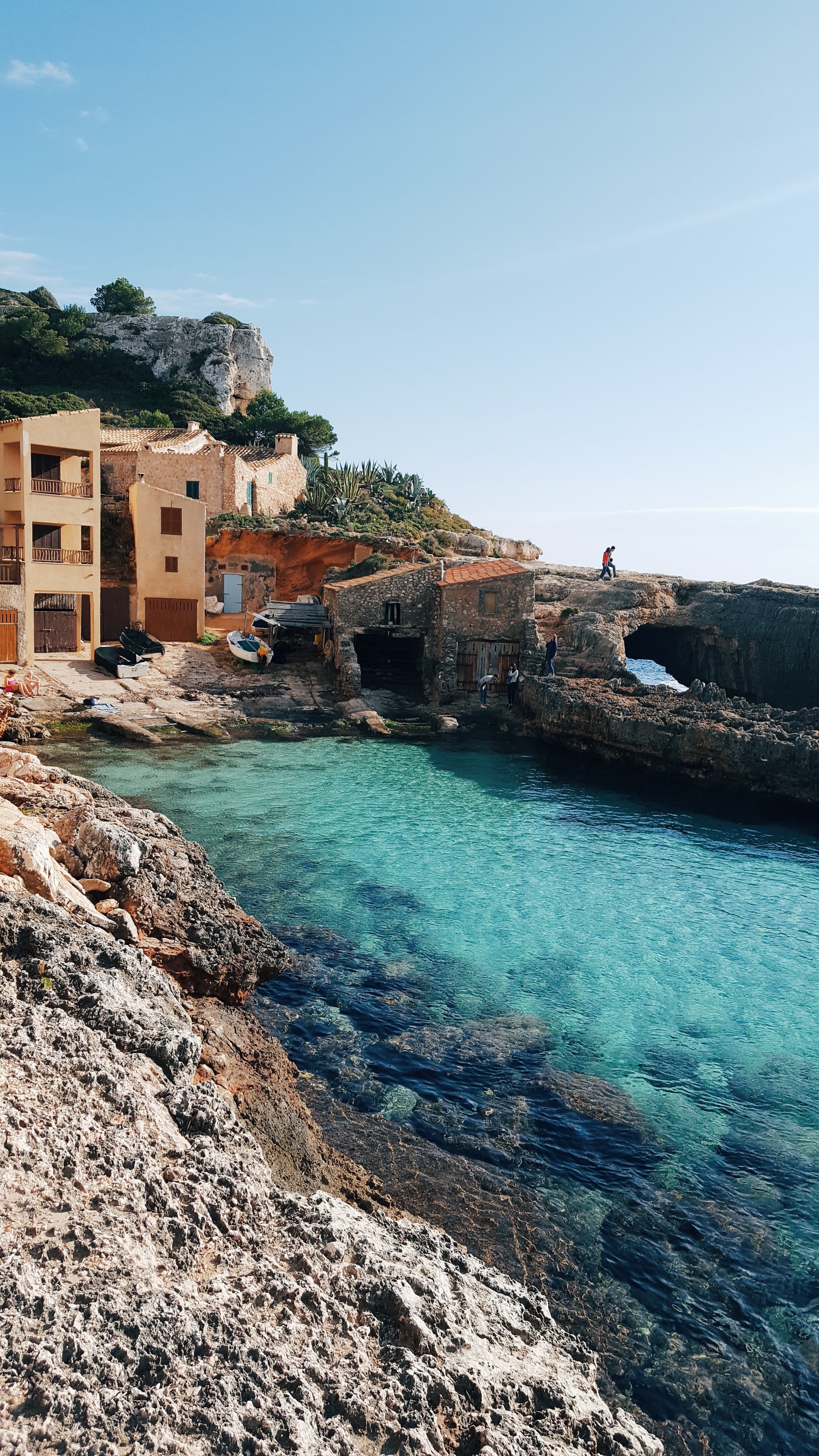 Tan buildings on top of seaside cliffs by serene turquoise waters in Mallorca, Spain.