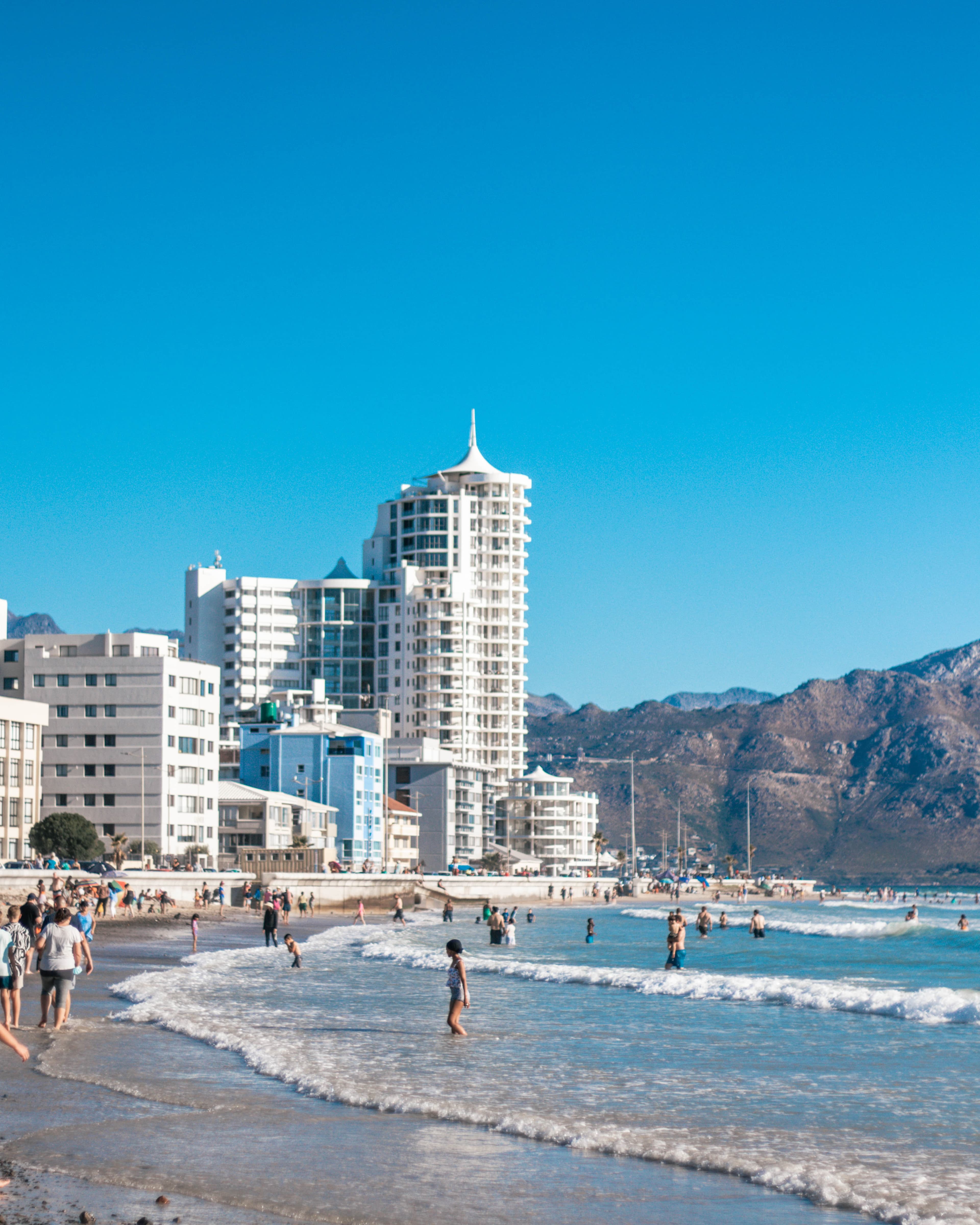 cape town south africa beach and city view of white buildings with people in the waves brown cliffs and blue water