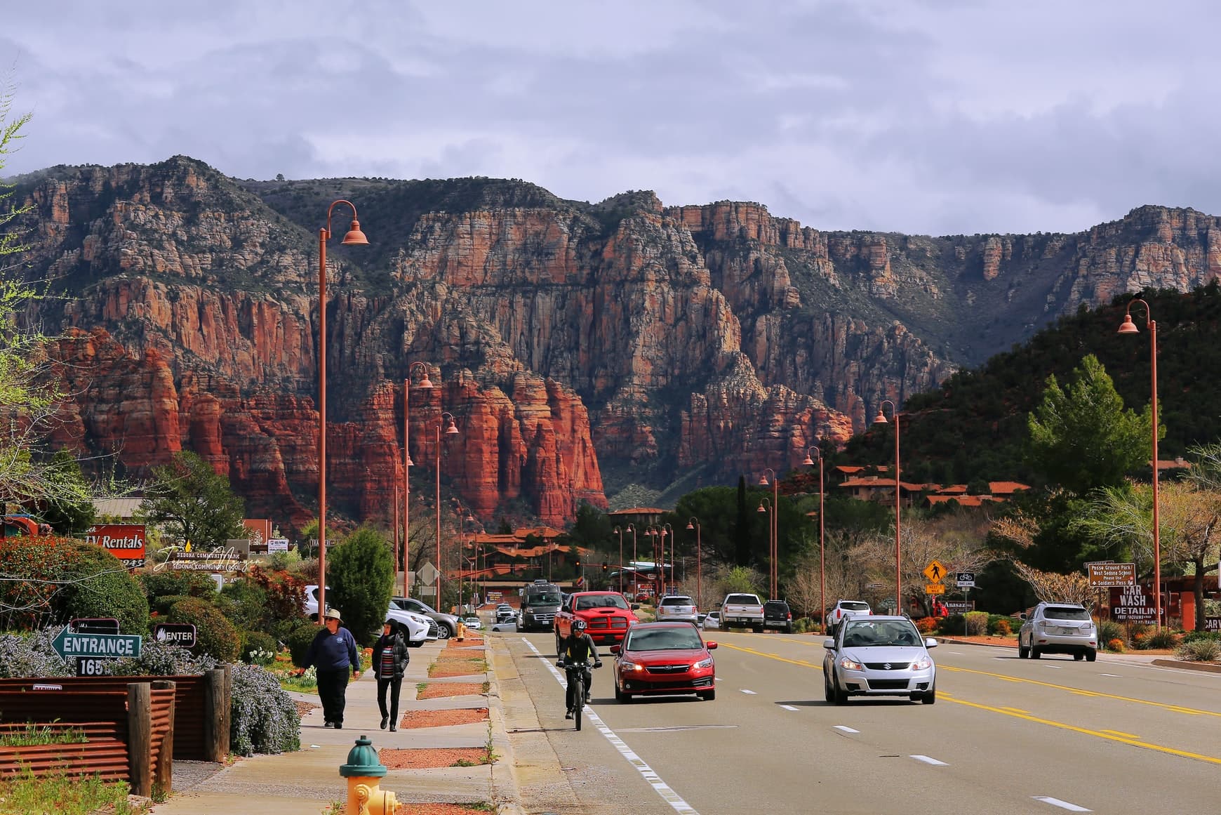 Sedona Arizona red clay mountains street with red and silver cars tall red lights and people walking and biking dressed