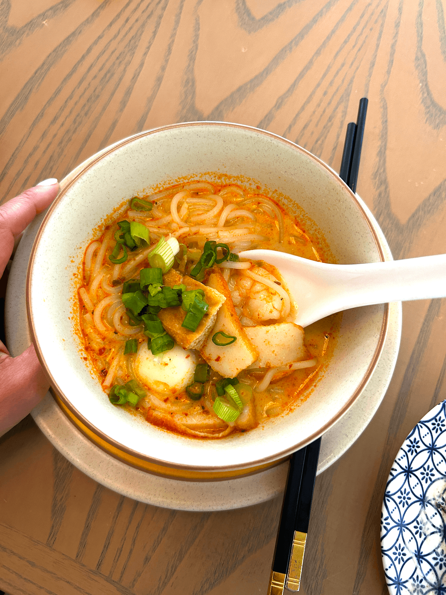 Noodle soup in a white bowl sitting on a wooden table