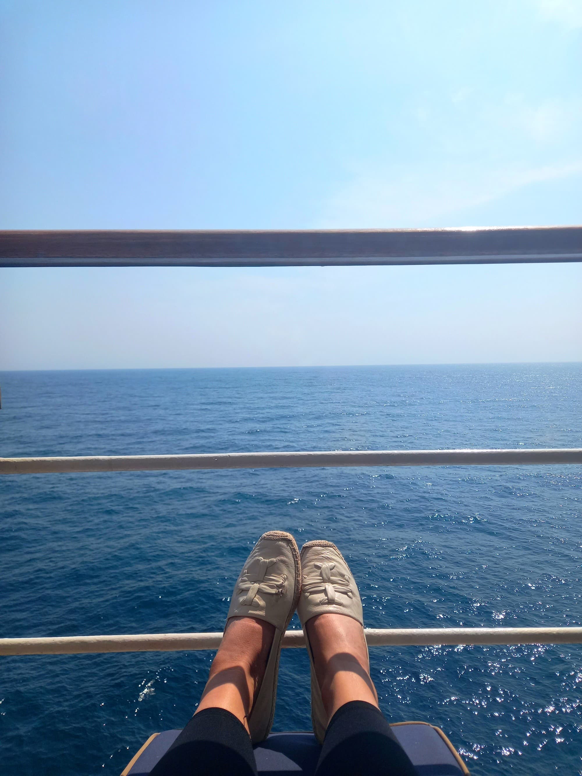 Feet in front of a ship railing with the ocean behind.